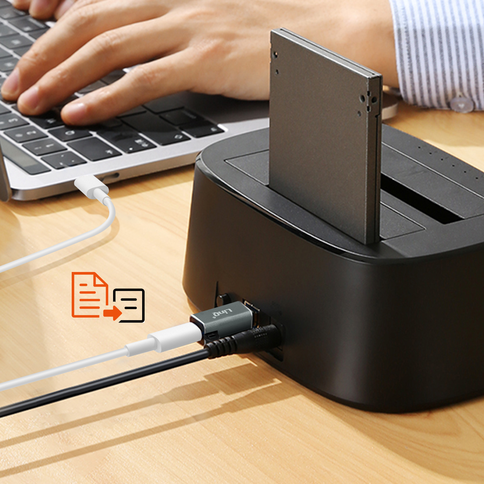 Una persona usa un laptop, con una docking station per disco rigido collegata a un computer con un cavo bianco e un cavo nero.
