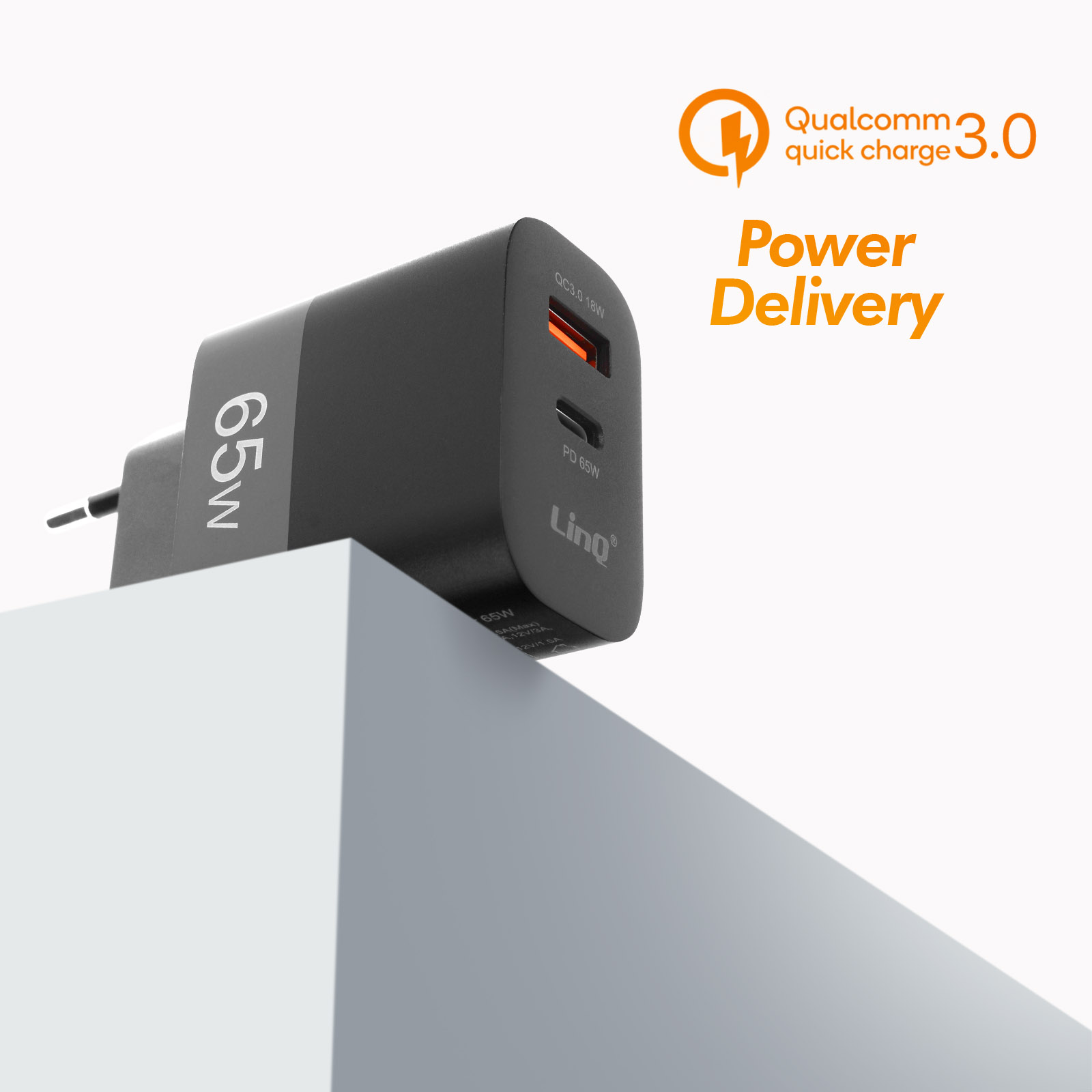 Un cargador negro de 65W con etiquetas QC 3.0 y Power Delivery naranjas, sobre superficie blanca inclinada.