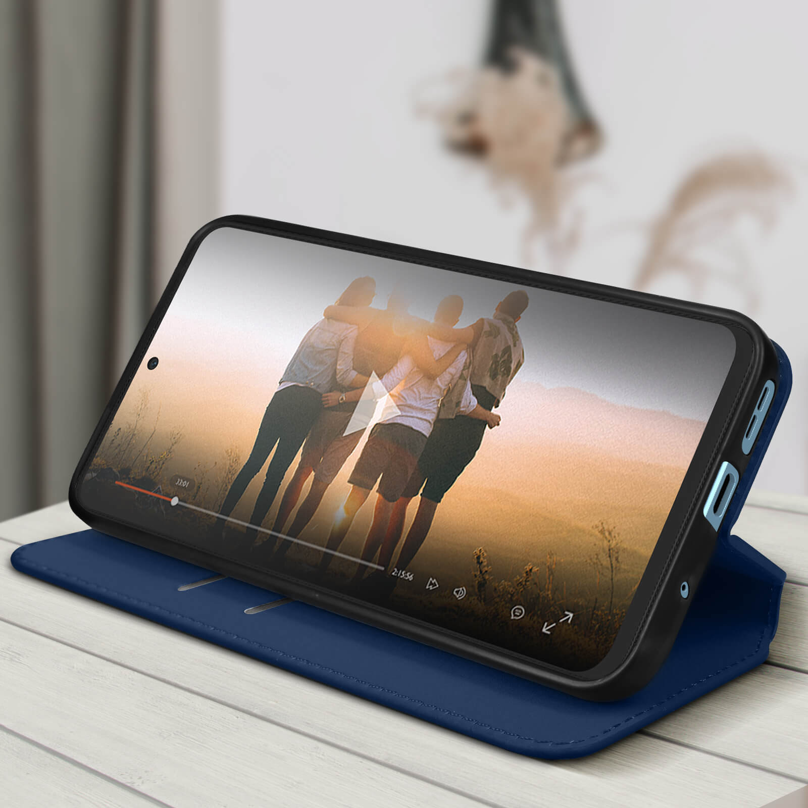 Uno smartphone che mostra un video è in una custodia blu, aperto su un tavolo.