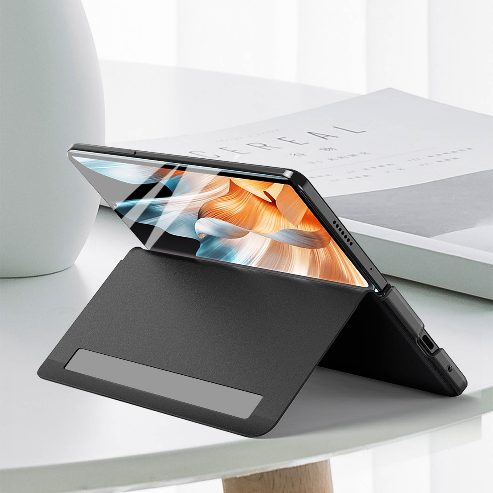 Custodia nera per tablet con tablet all'interno, su superficie bianca con libro.