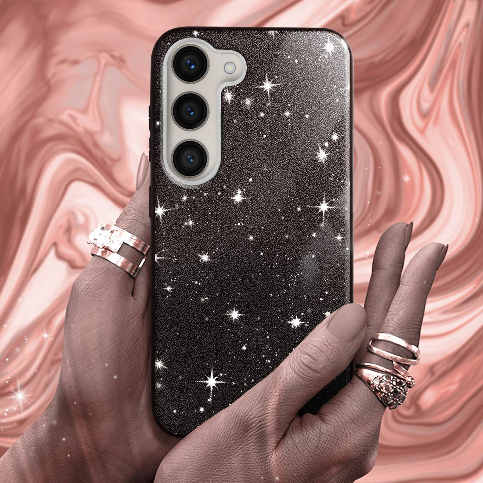 Una mano che tiene un telefono in una custodia scintillante. Ci sono anelli alle dita e uno sfondo rosa.