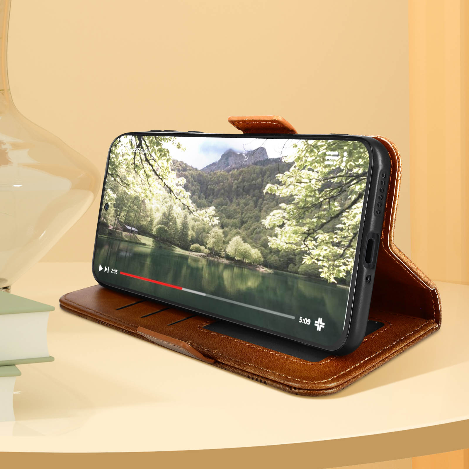 Telefono in custodia marrone che mostra un video di un lago e alberi. La custodia è su un tavolo.