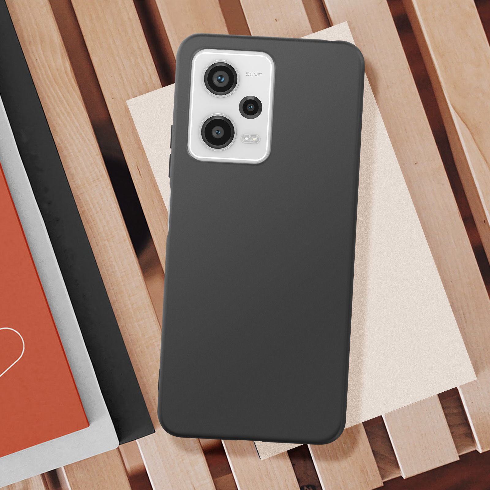 Telefono nero con custodia nera, appoggiato su assi di legno e un pezzo di carta bianca.