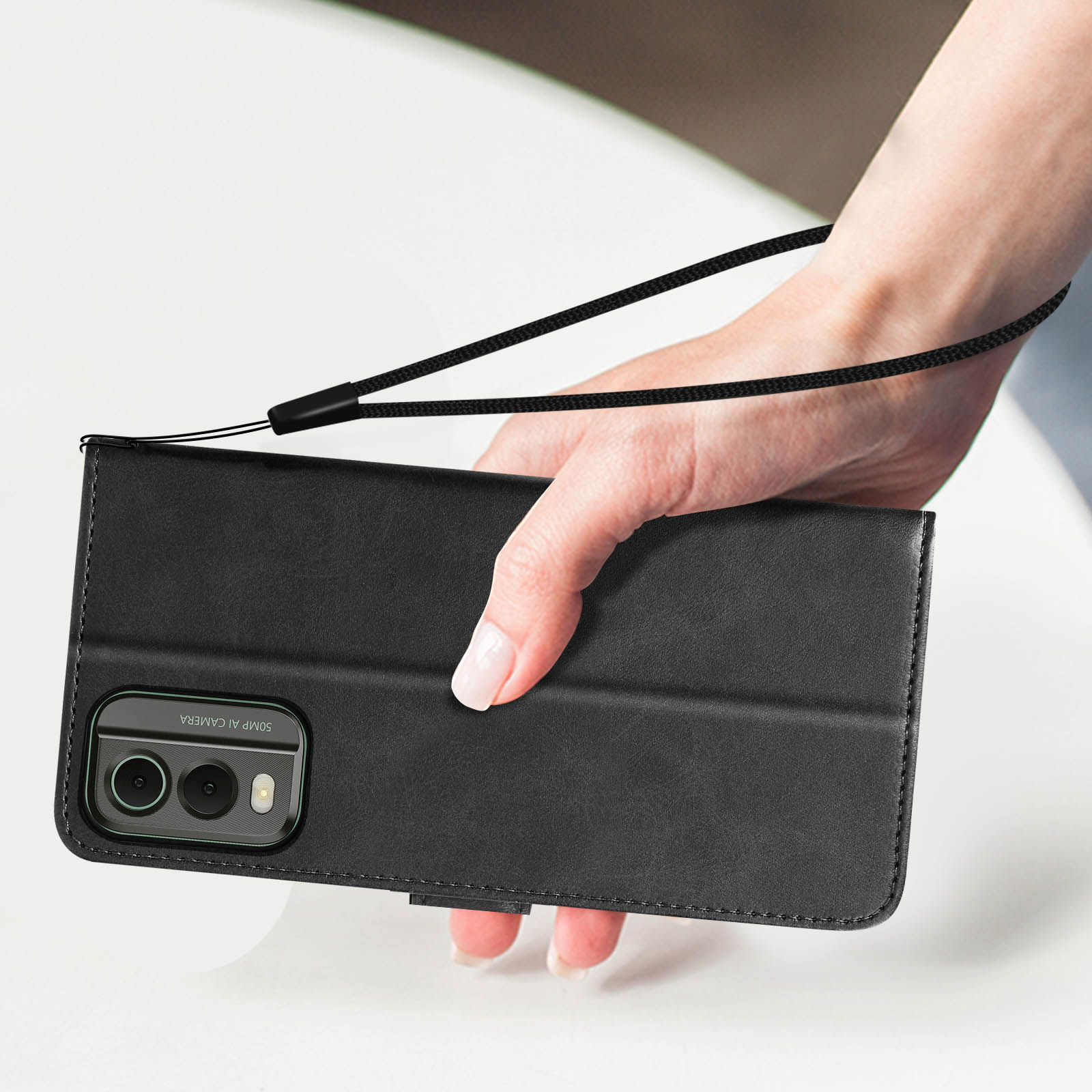Mano che tiene una custodia per telefono in pelle nera con cinturino. Visibile un telefono a doppia fotocamera.