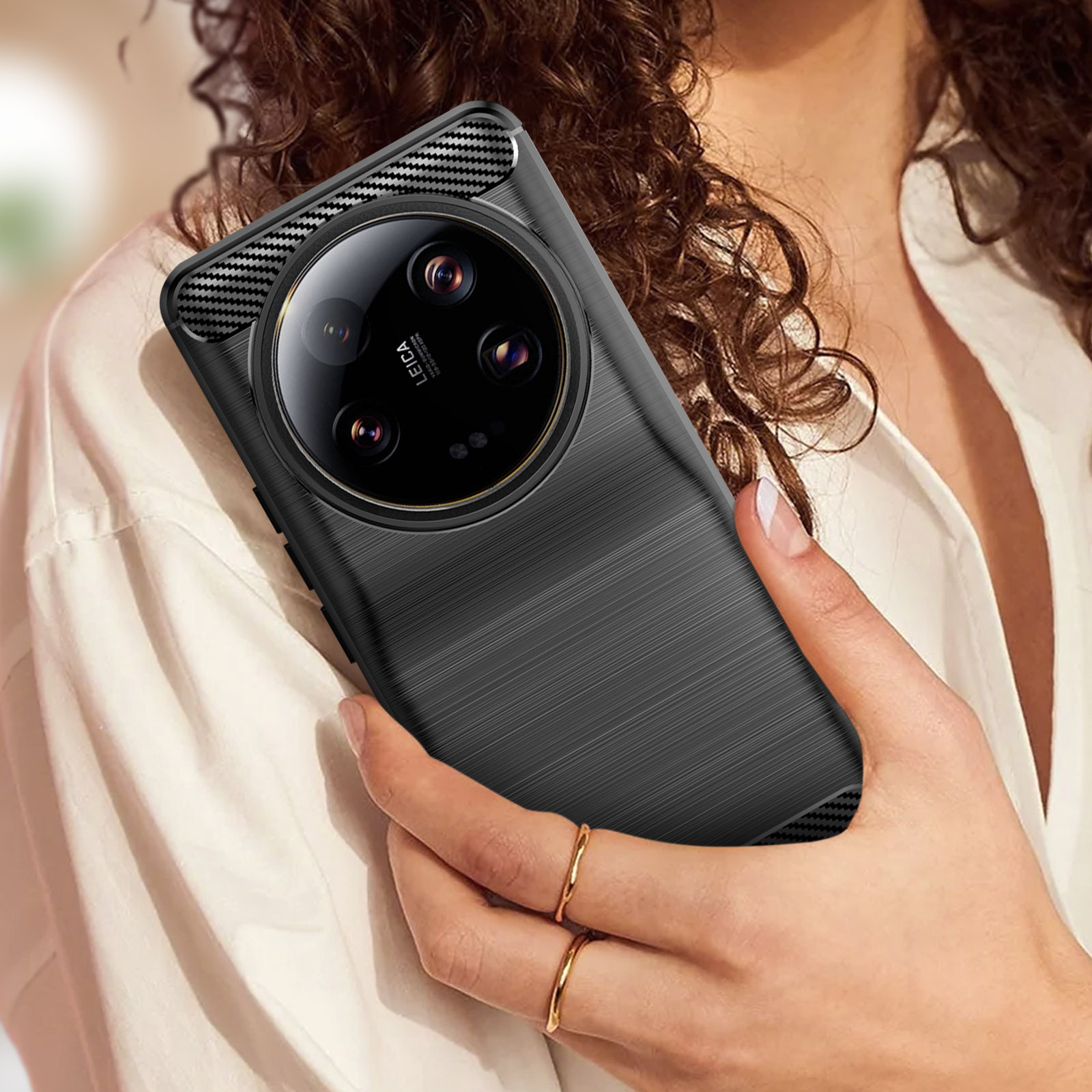 Telefono nero con custodia, mano che lo tiene. Camicia bianca, sfondo grigio.