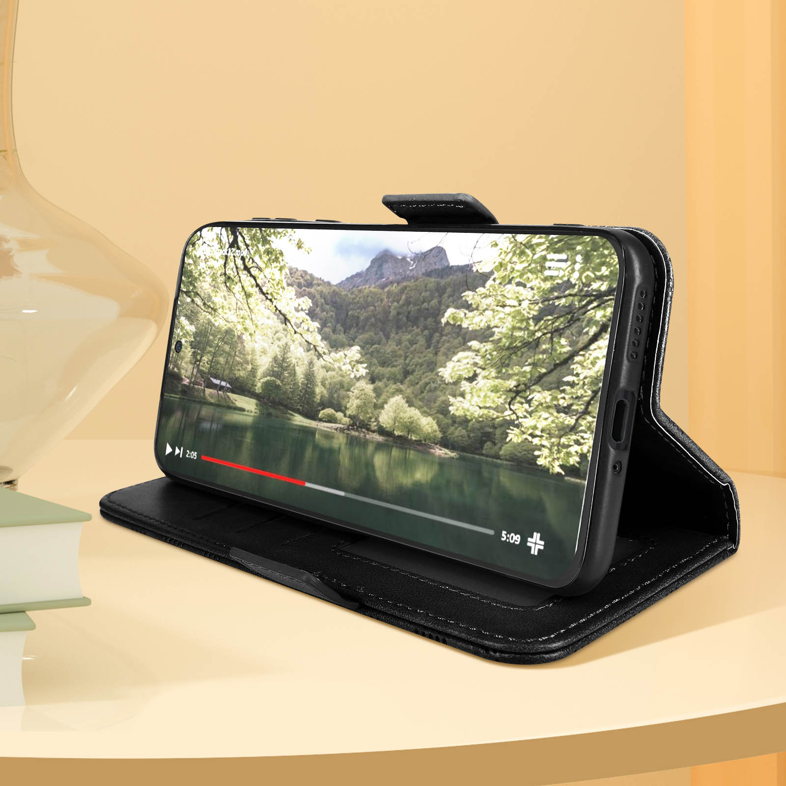 Custodia nera per telefono aperta, che mostra un video sullo schermo del telefono, con uno sfondo naturale.