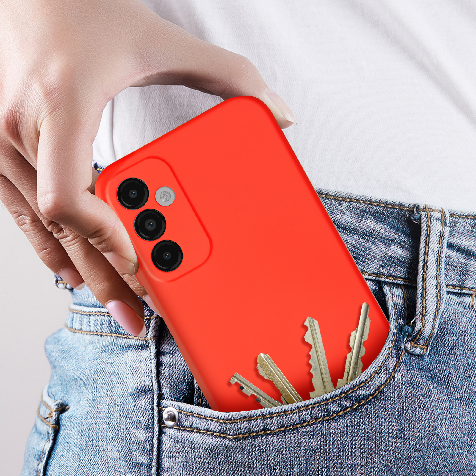 Una mano che tiene un telefono rosso in tasca con delle chiavi. Tasca dei jeans visibile.