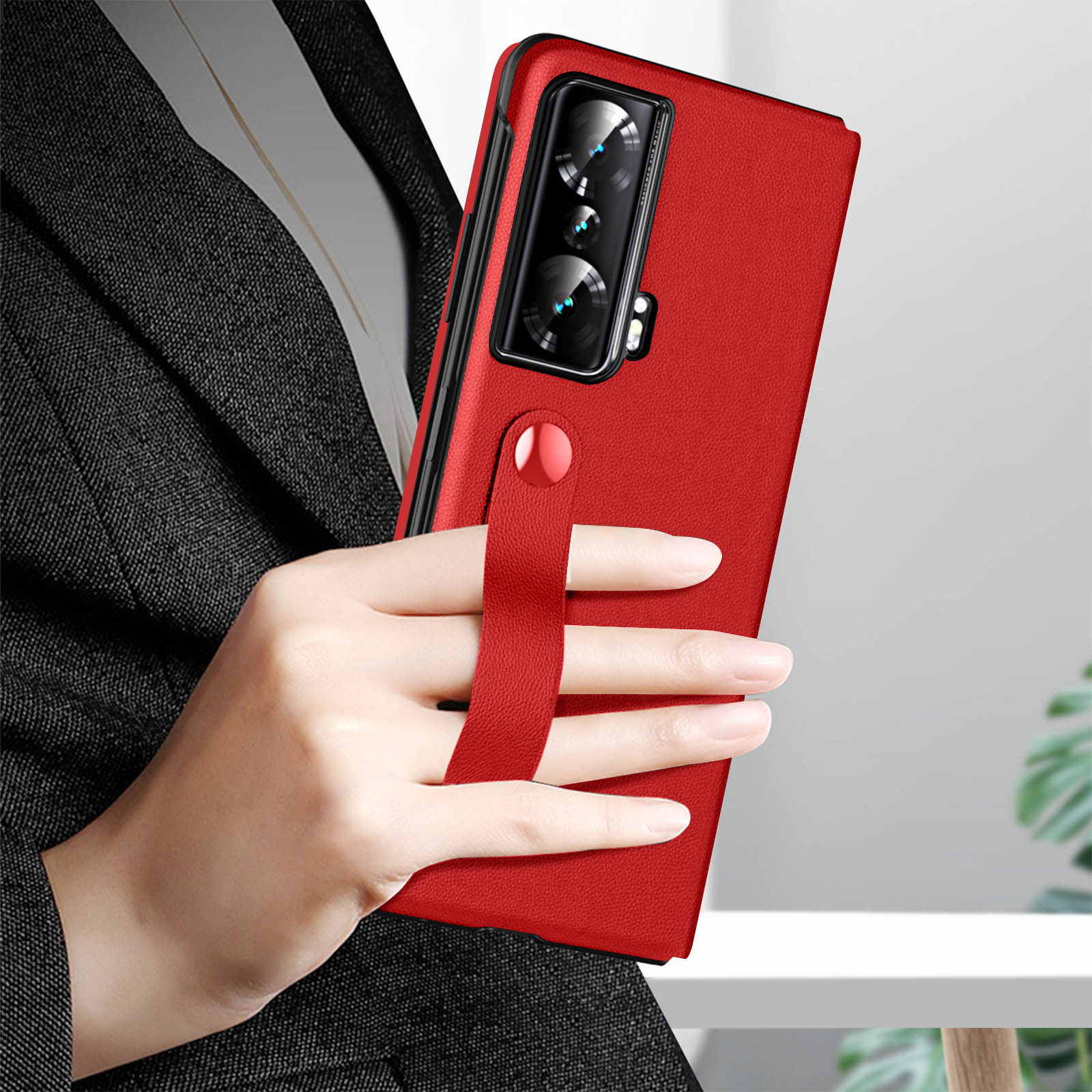Persona che tiene un telefono rosso in una custodia con cinturino. Lo sfondo è un abito scuro.