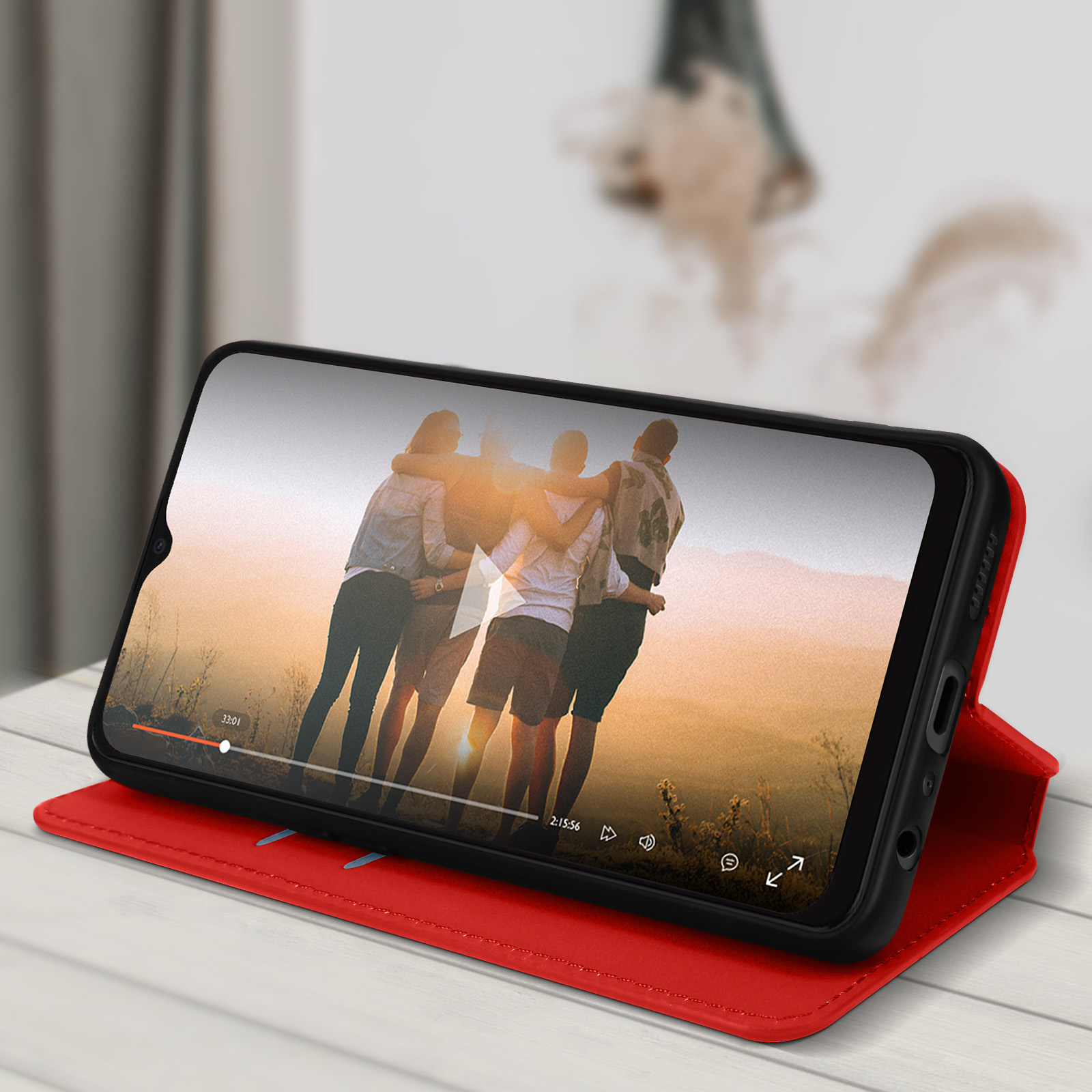 Telefono con video in riproduzione, in una custodia rossa, su una superficie di legno.