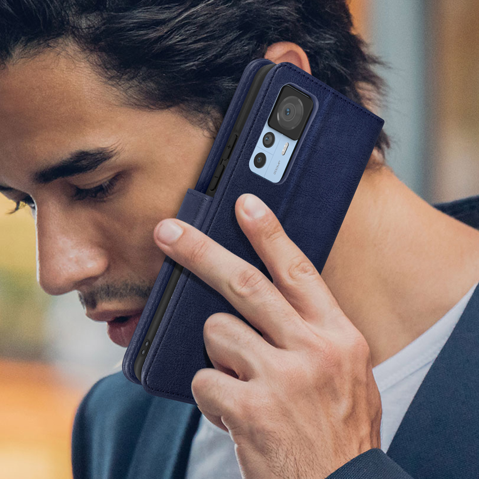Mann hält Telefon ans Ohr, in blauer Hülle. Er trägt einen Blazer.