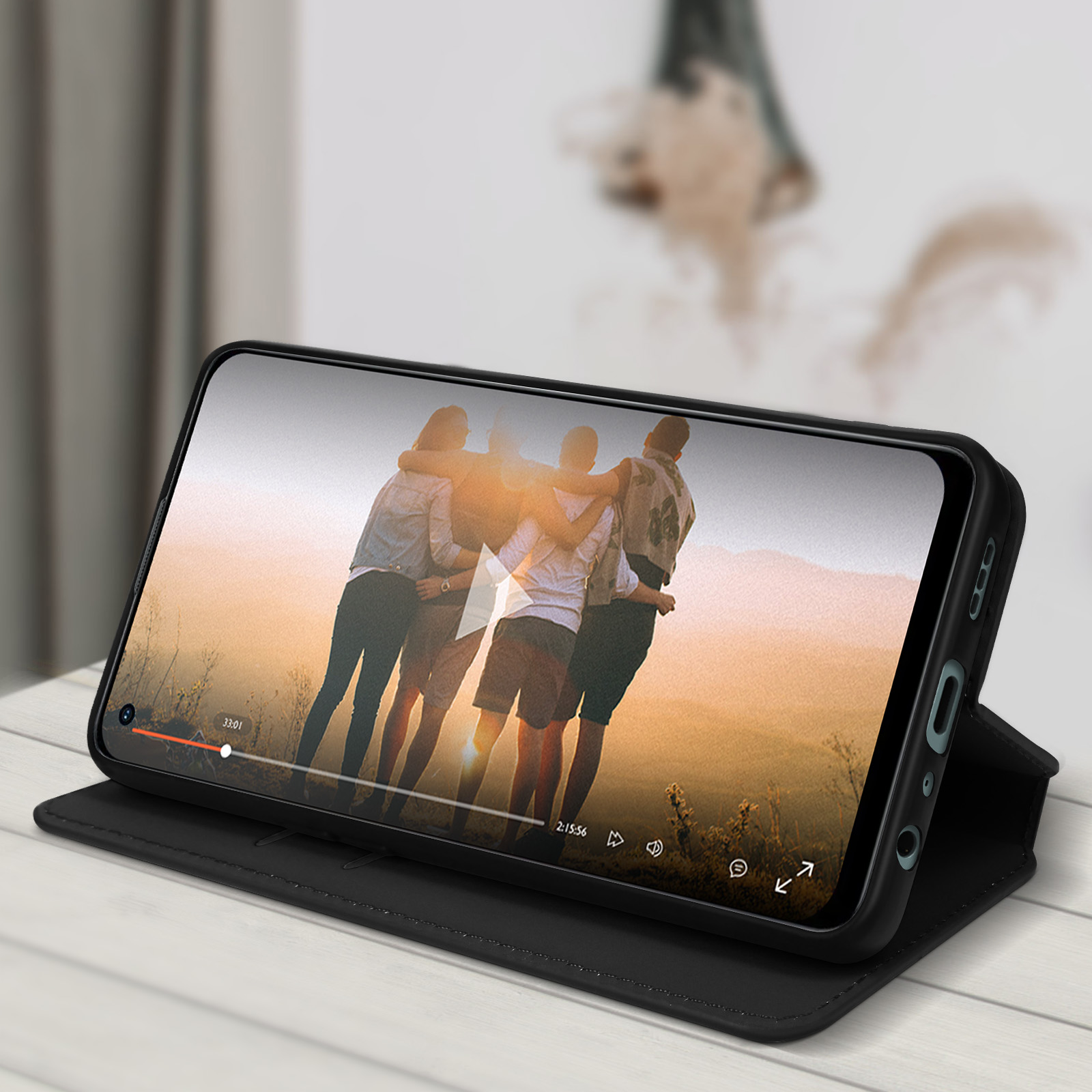 Un telefono in una custodia, che mostra un video di persone che si abbracciano al tramonto, su una superficie nera.