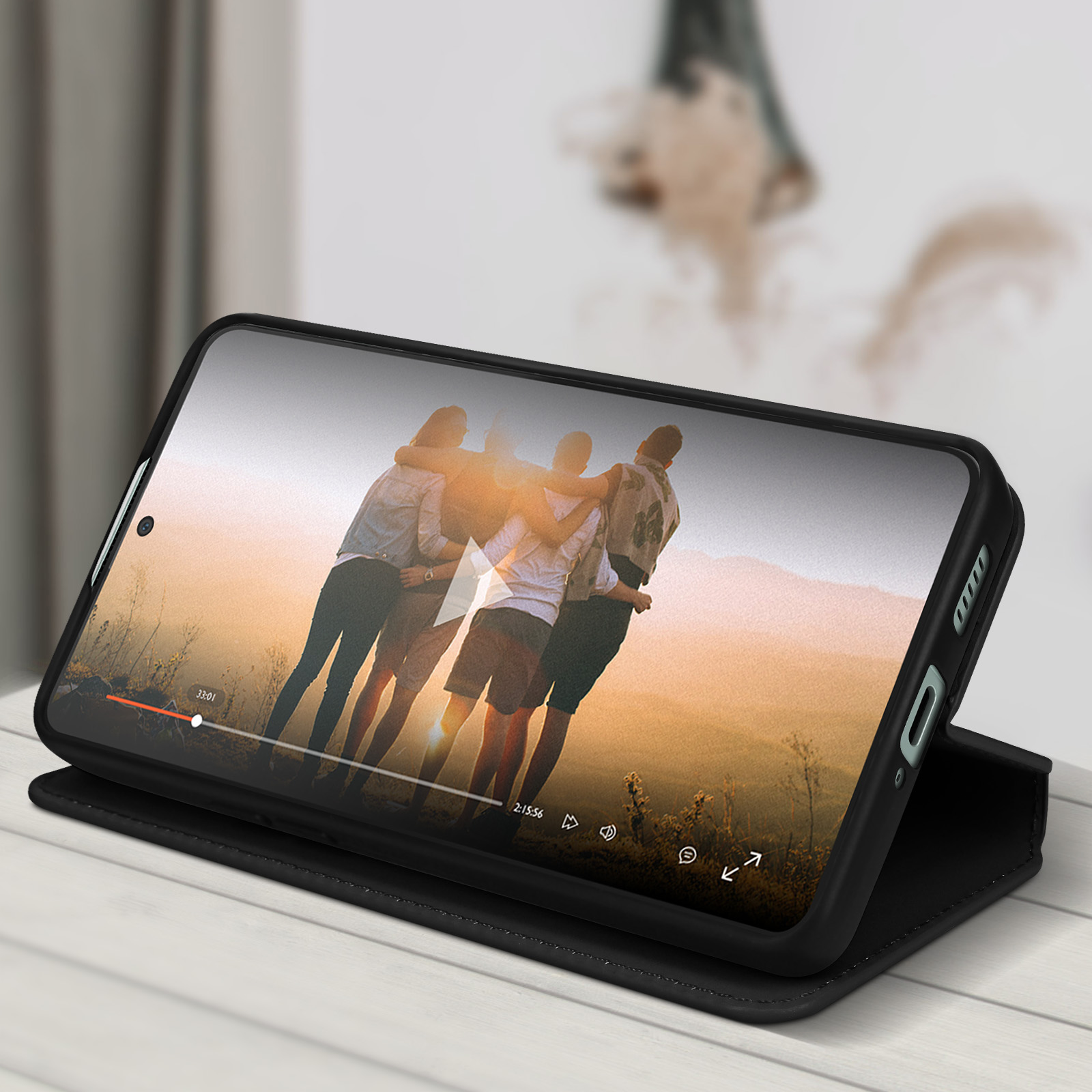 Telefon zeigt Video von umarmenden Menschen, auf Tisch, lederartige Hülle offen.