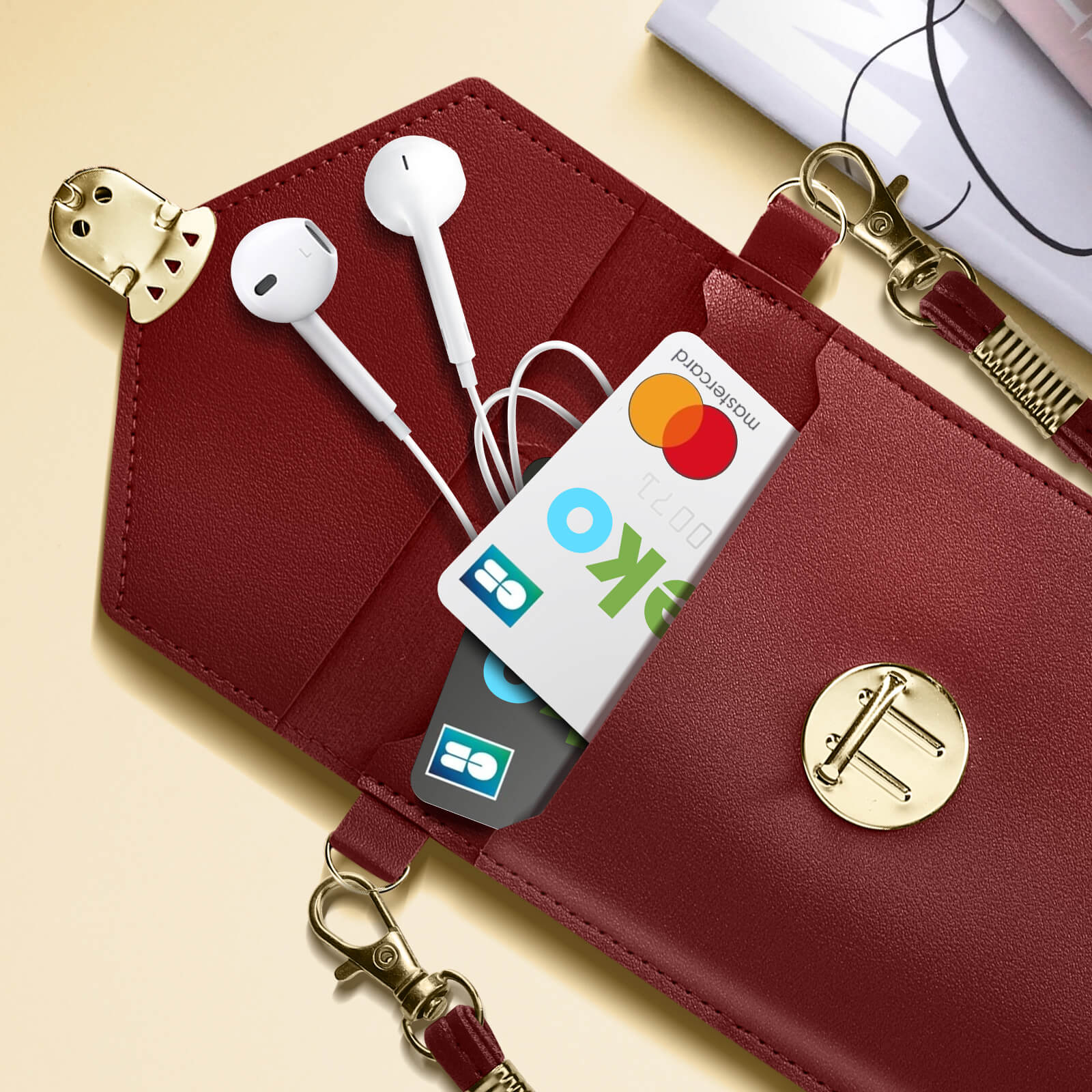 Burgunderfarbene Hülle mit Ohrhörern, Karte und goldfarbener Hardware. Weiße Ohrhörer in der Hülle. Mastercard in der Hülle.