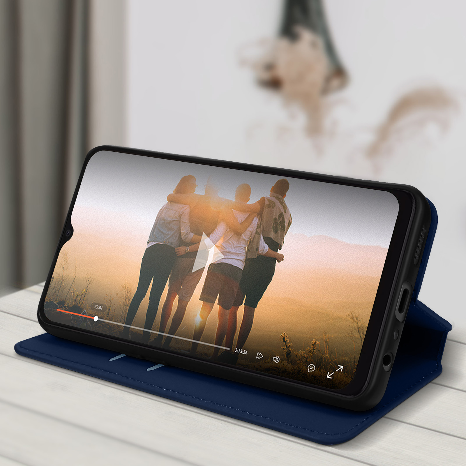 Un telefono che riproduce un video di persone che si abbracciano, in una custodia blu su un tavolo bianco.