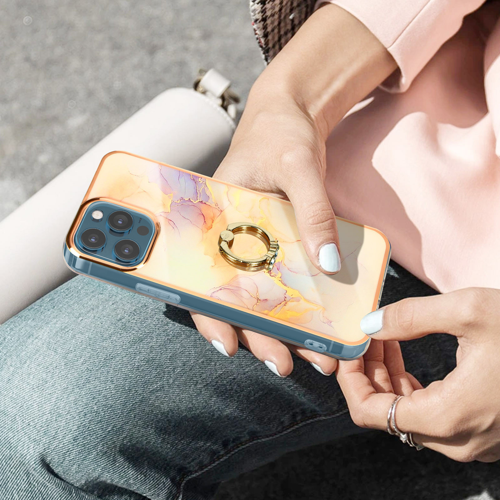 Manos sosteniendo un teléfono con una funda colorida. La funda tiene un soporte de anillo. El fondo está borroso.