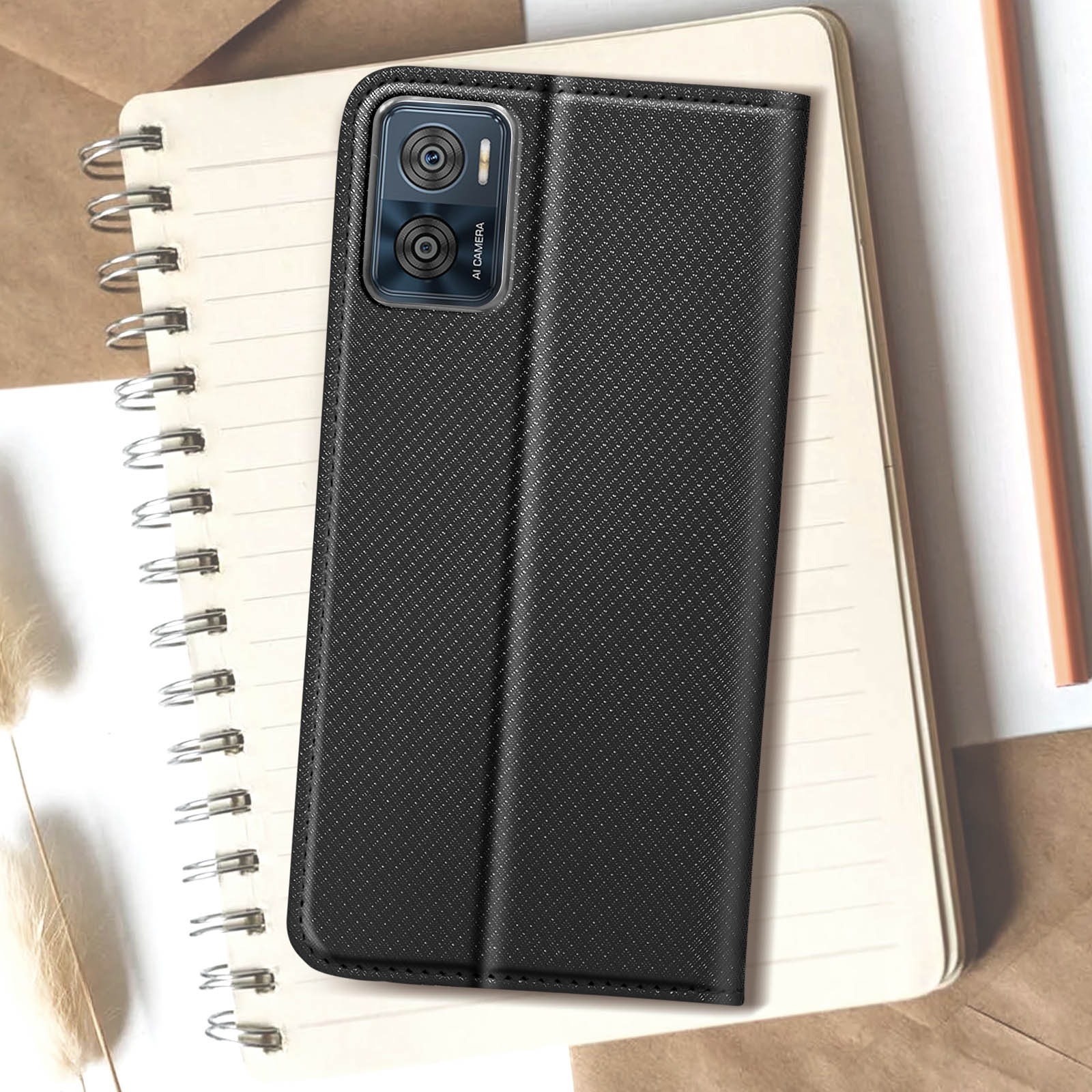 Eine schwarze Handyhülle mit strukturiertem Muster liegt auf einem Notizbuch. Die Hülle ist geöffnet und zeigt ein Telefon.