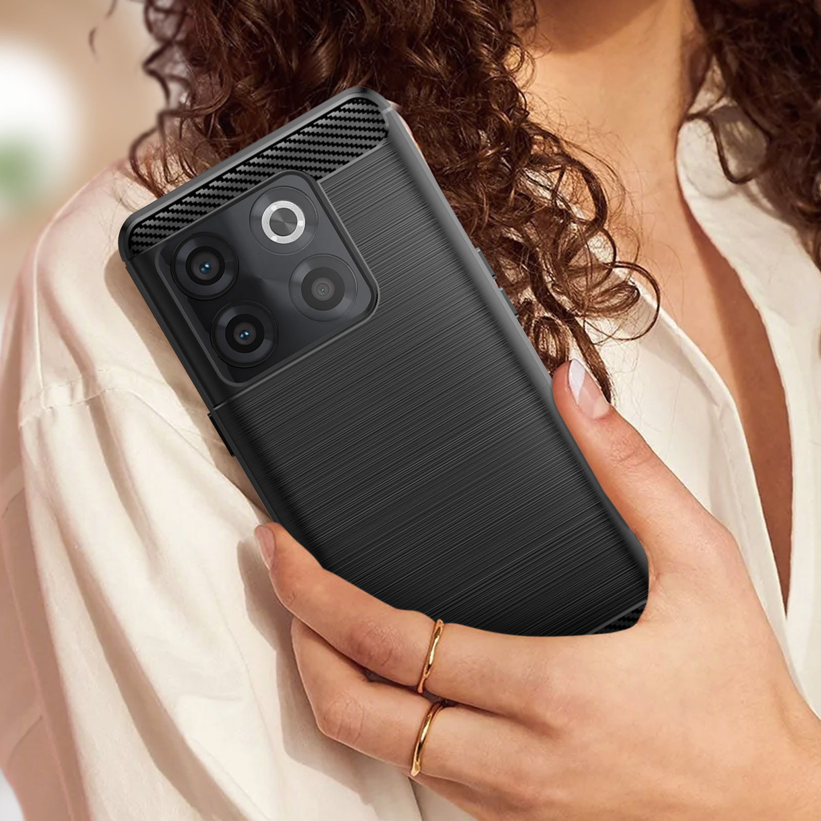 Hände einer Frau halten ein schwarzes Telefon mit strukturierter Hülle. Ringe sichtbar. Nahaufnahme.