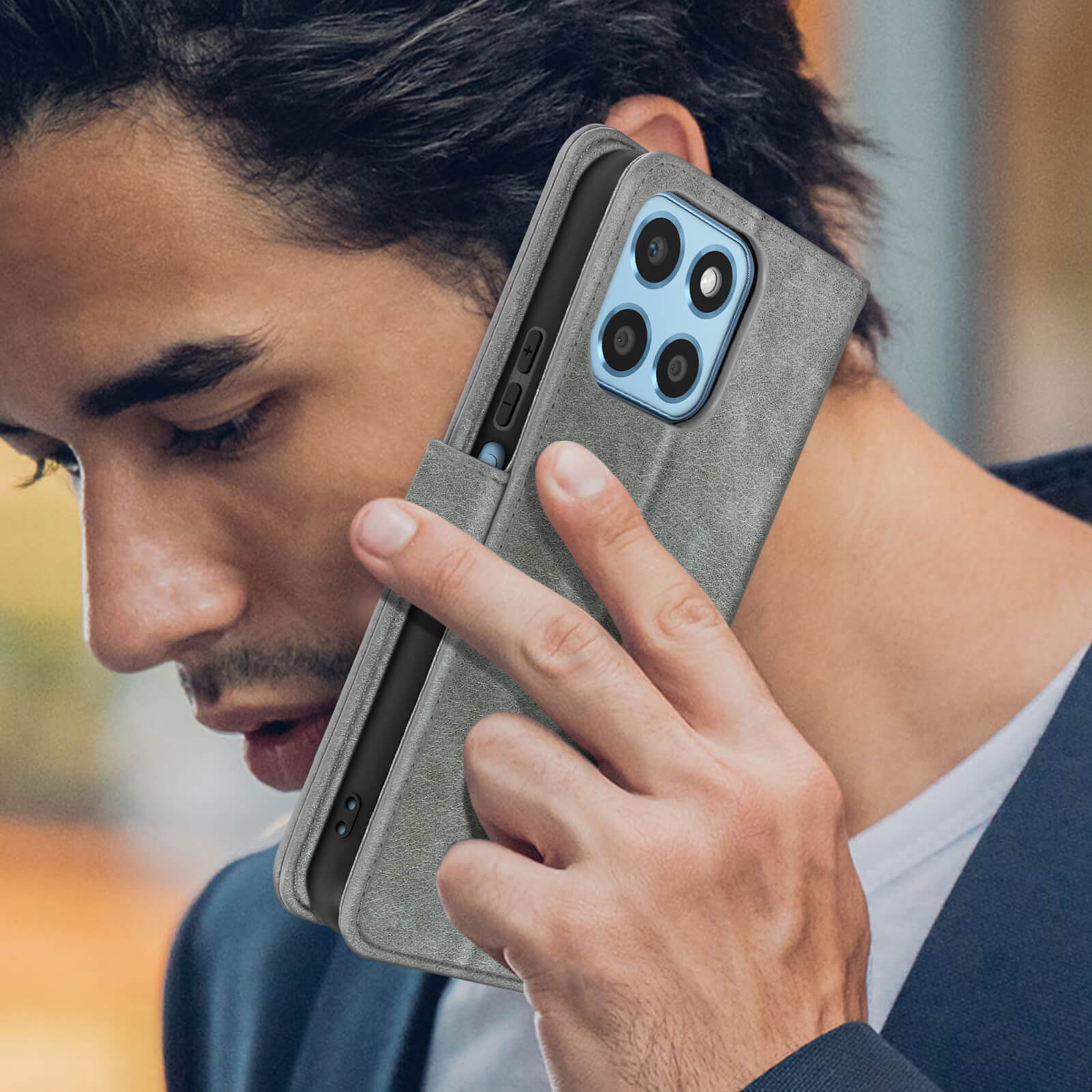 Mann hält eine graue Handyhülle mit einem Telefon darin. Der Mann trägt einen Blazer und ein weißes Hemd.