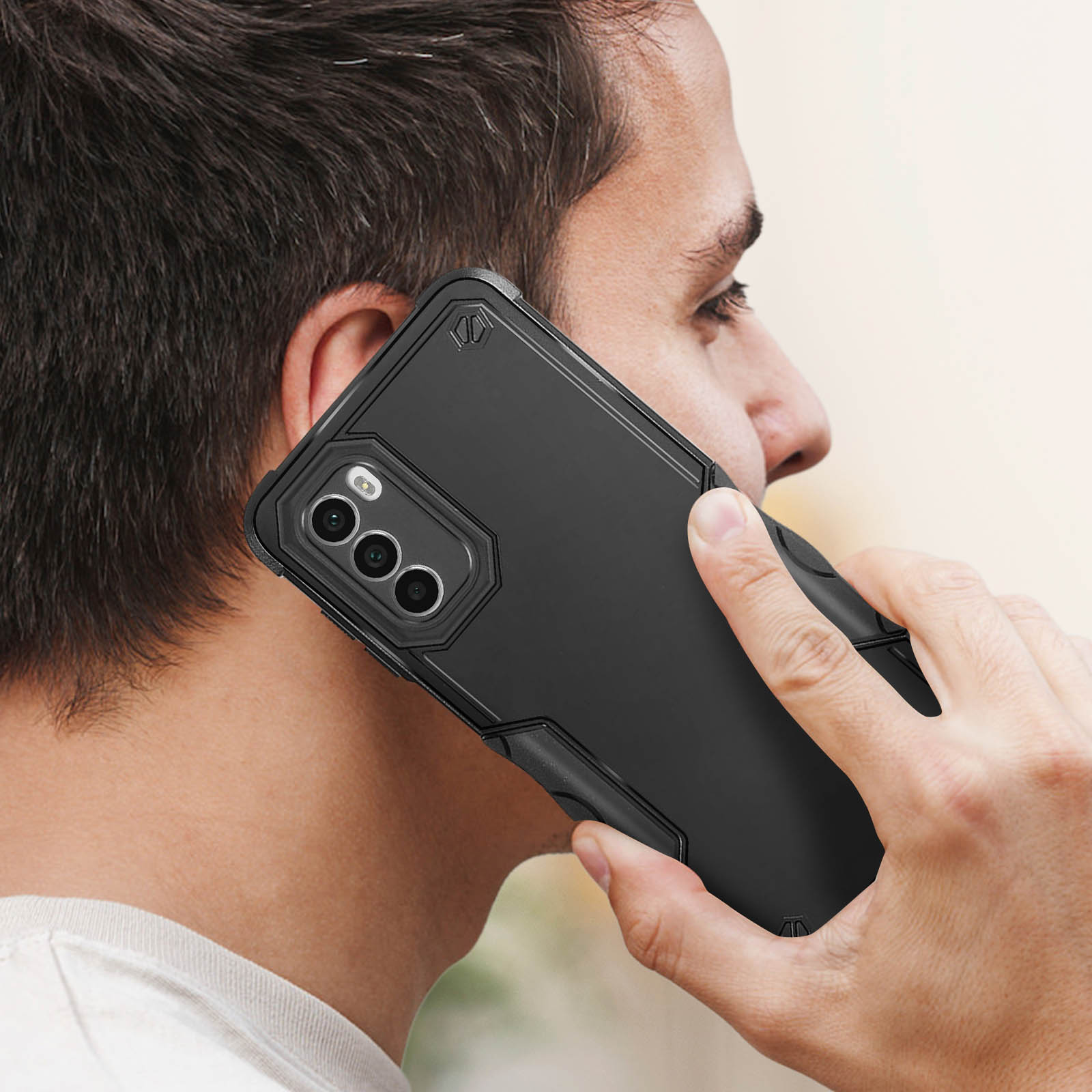 Una persona che tiene un telefono nero con una custodia all'orecchio. La persona è di profilo.