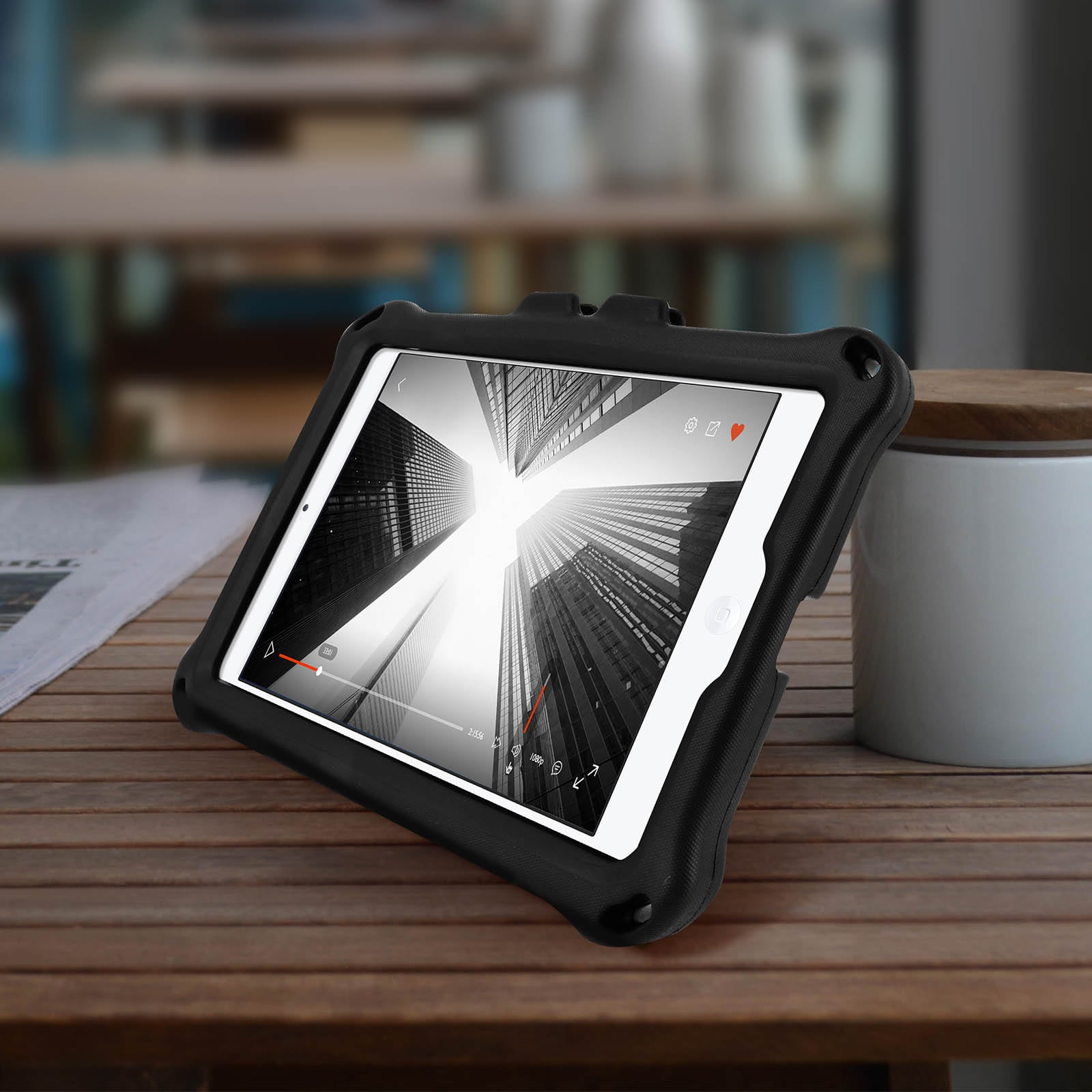 Ein Tablet in einer schwarzen Hülle, das ein Video anzeigt. Das Tablet liegt auf einem Holztisch neben einem weißen Glas.