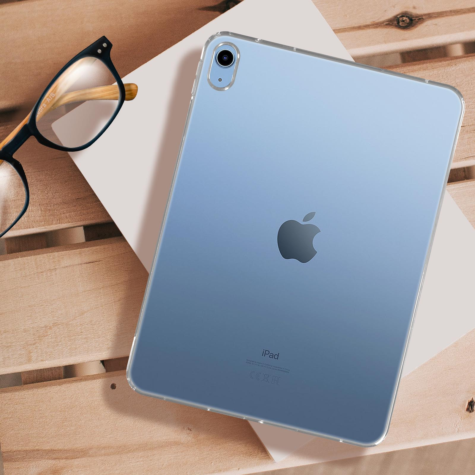 Blaues iPad auf Holzoberfläche, mit klarer Hülle und Brille in der Nähe.