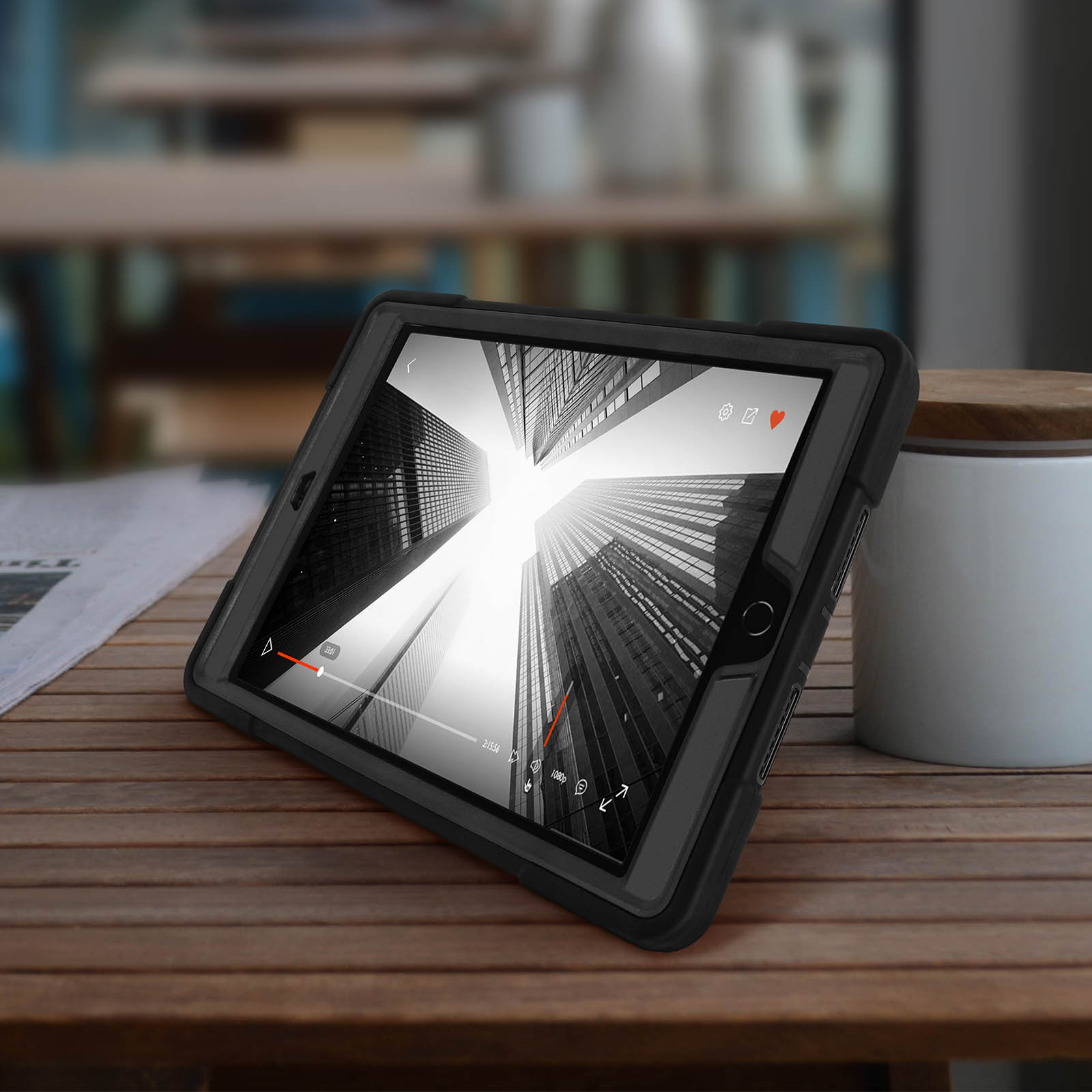 Tablet in schwarzer Hülle auf Holztisch, spielt Video. Hintergrund unscharf.