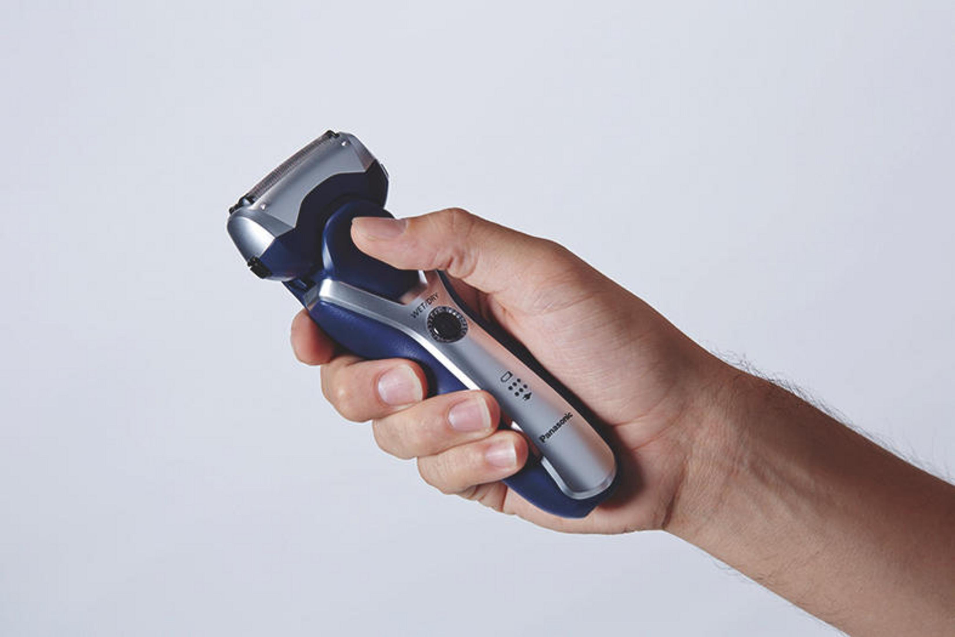 Männerhand hält Elektrorasierer. Blaues und silbernes Farbschema, Nahaufnahme.