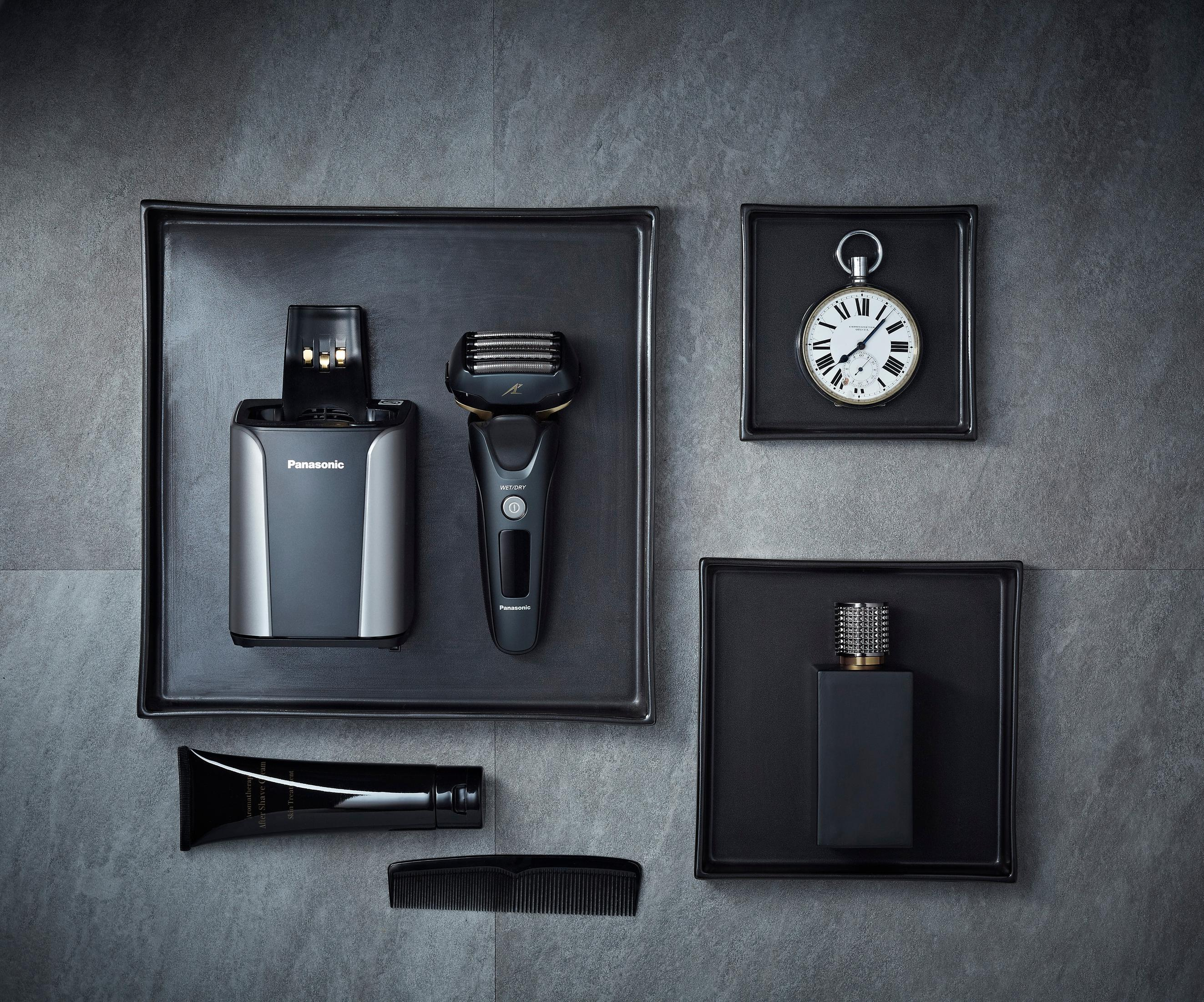 Eine Sammlung von Pflegeartikeln: Rasierer, Ladegerät, Creme, Kamm und eine Taschenuhr.
