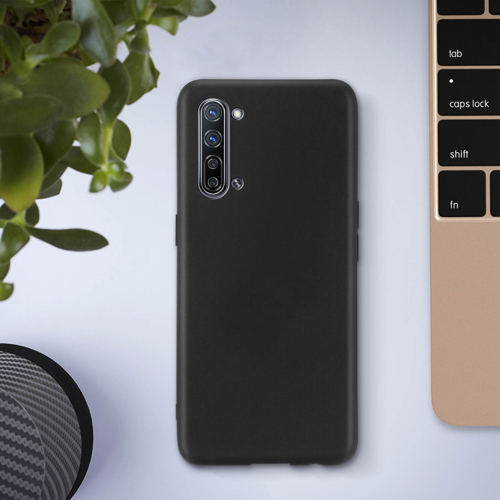 Une coque de téléphone noire sur un bureau avec une plante et un ordinateur portable. La coque a une découpe pour l'appareil photo.