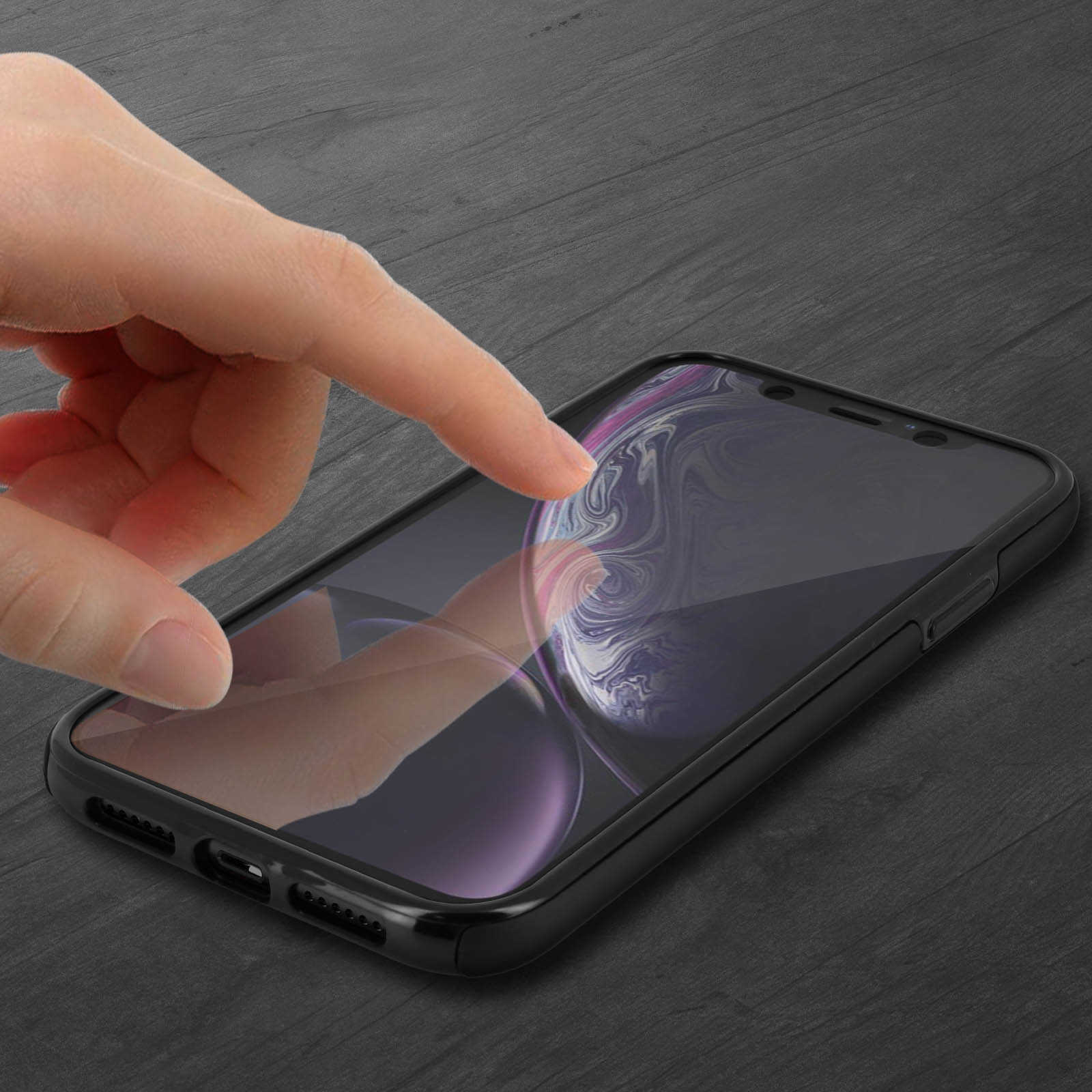 Mano che tocca lo schermo di un telefono in una custodia nera, su superficie in legno scuro.