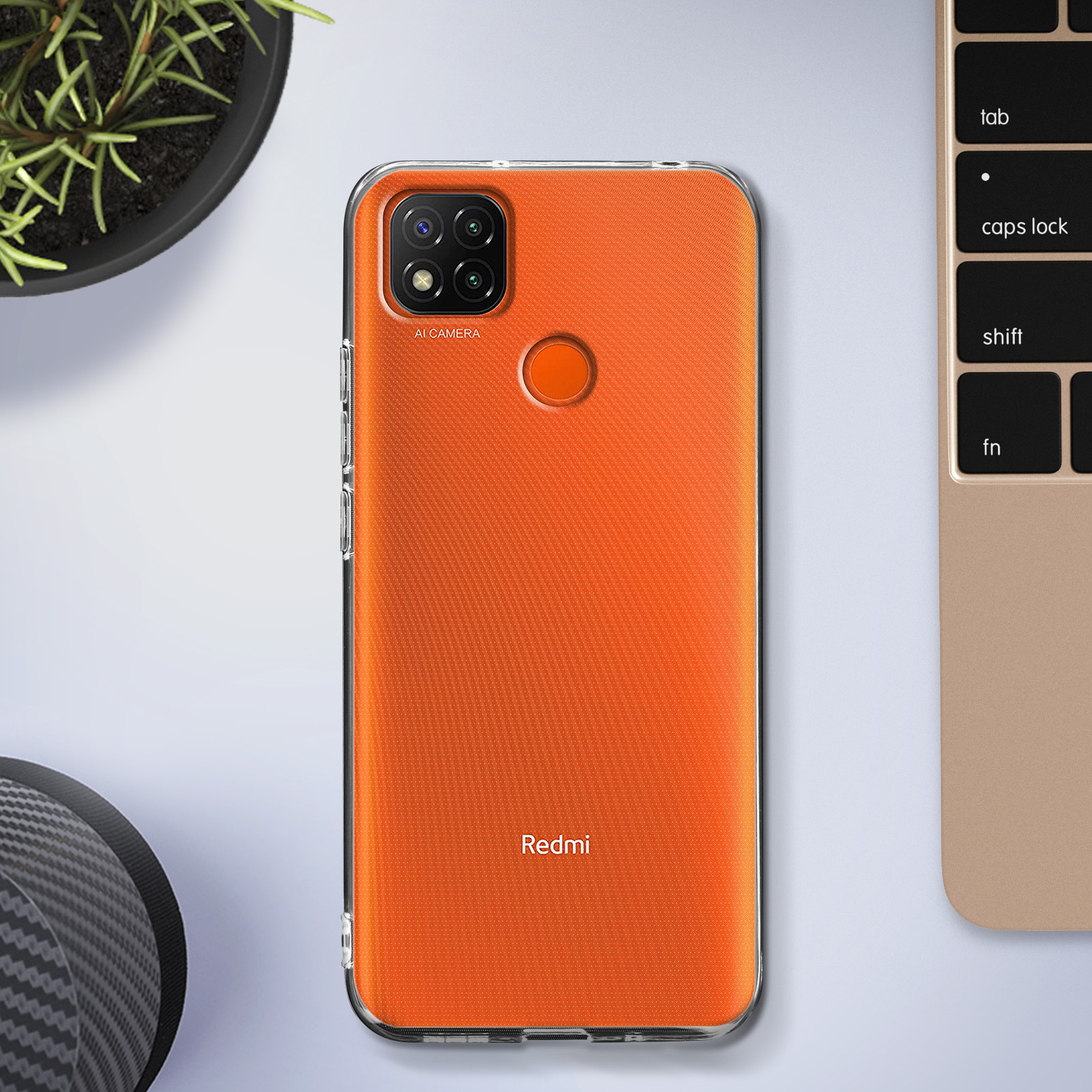 Een oranje telefoonhoesje op een tafel. Er staat een laptop en een plant op de achtergrond.