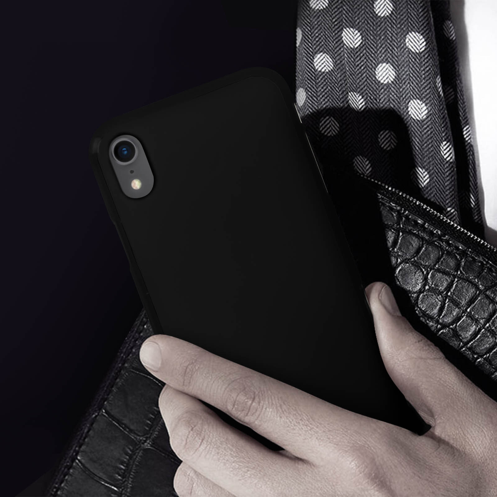 Ein schwarzes Telefon in einer schwarzen Hülle, gehalten von einer Person. Hintergrund: gemusterter Schal.