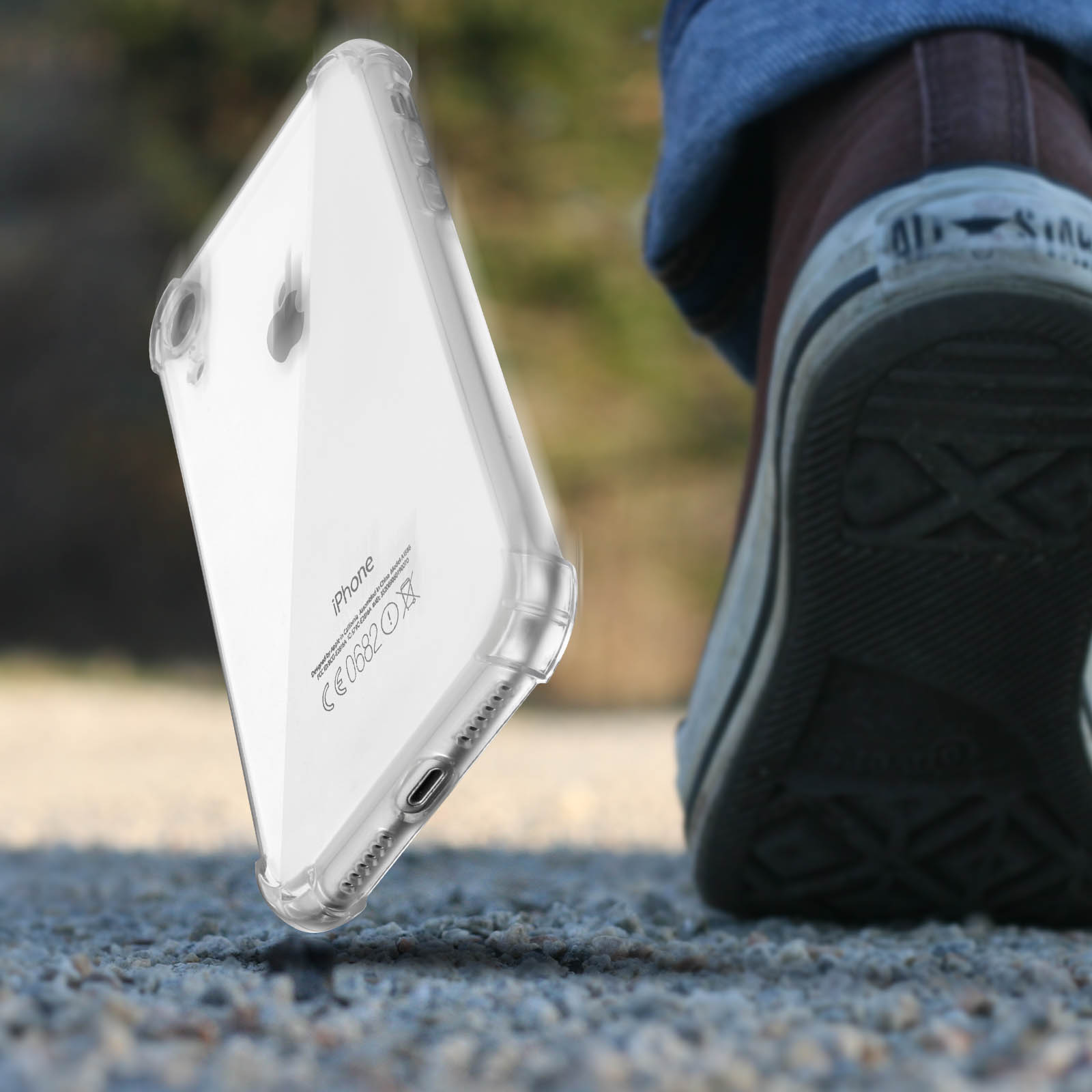 Custodia trasparente per telefono che cade a terra. Gamba e scarpa di una persona sullo sfondo.