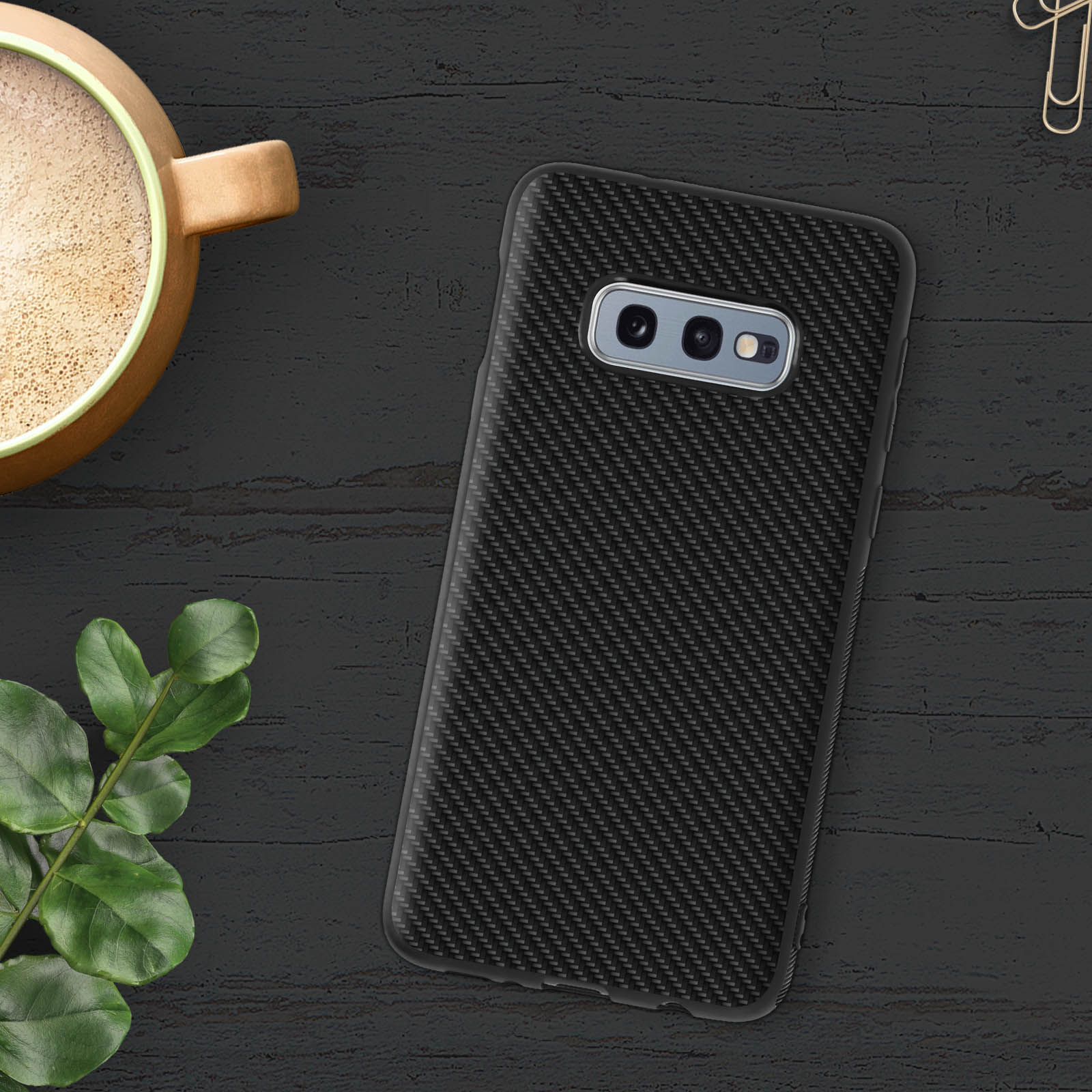 Un telefono nero in una custodia con texture in fibra di carbonio su una superficie di legno scuro. Tazza di caffè a sinistra.