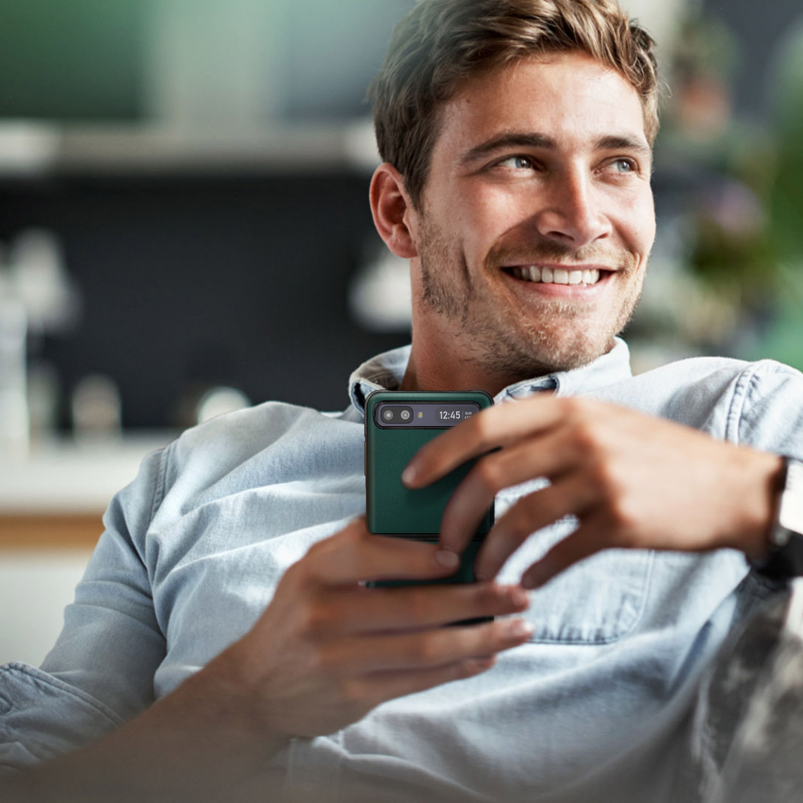 Uomo che tiene un telefono verde. Sta sorridendo ed è seduto su un divano. Il telefono mostra l'ora.