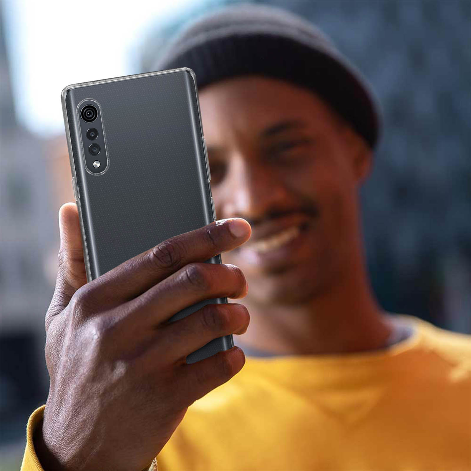 Persona che tiene in mano un telefono nero con custodia trasparente. Sorridente, sfondo sfocato.