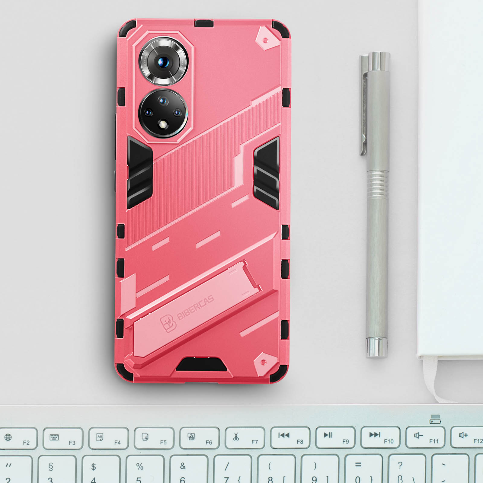 Custodia rosa per telefono su scrivania bianca con penna e tastiera. Ha un supporto.