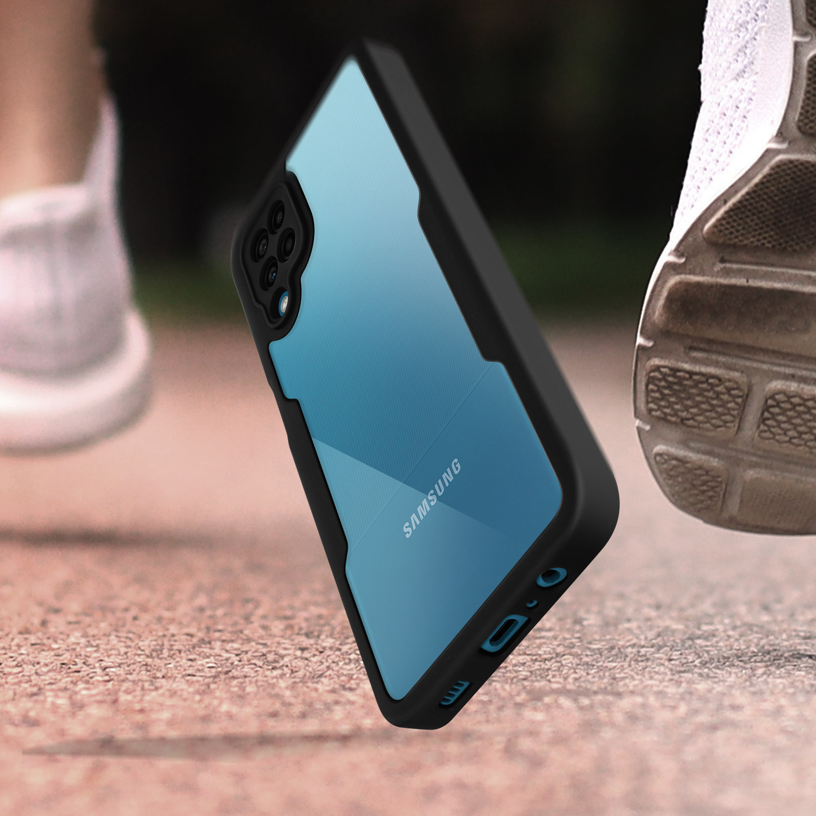 Een telefoon in een zwarte hoes hangt in de lucht. De benen en schoenen van een persoon zijn vaag zichtbaar op de achtergrond.