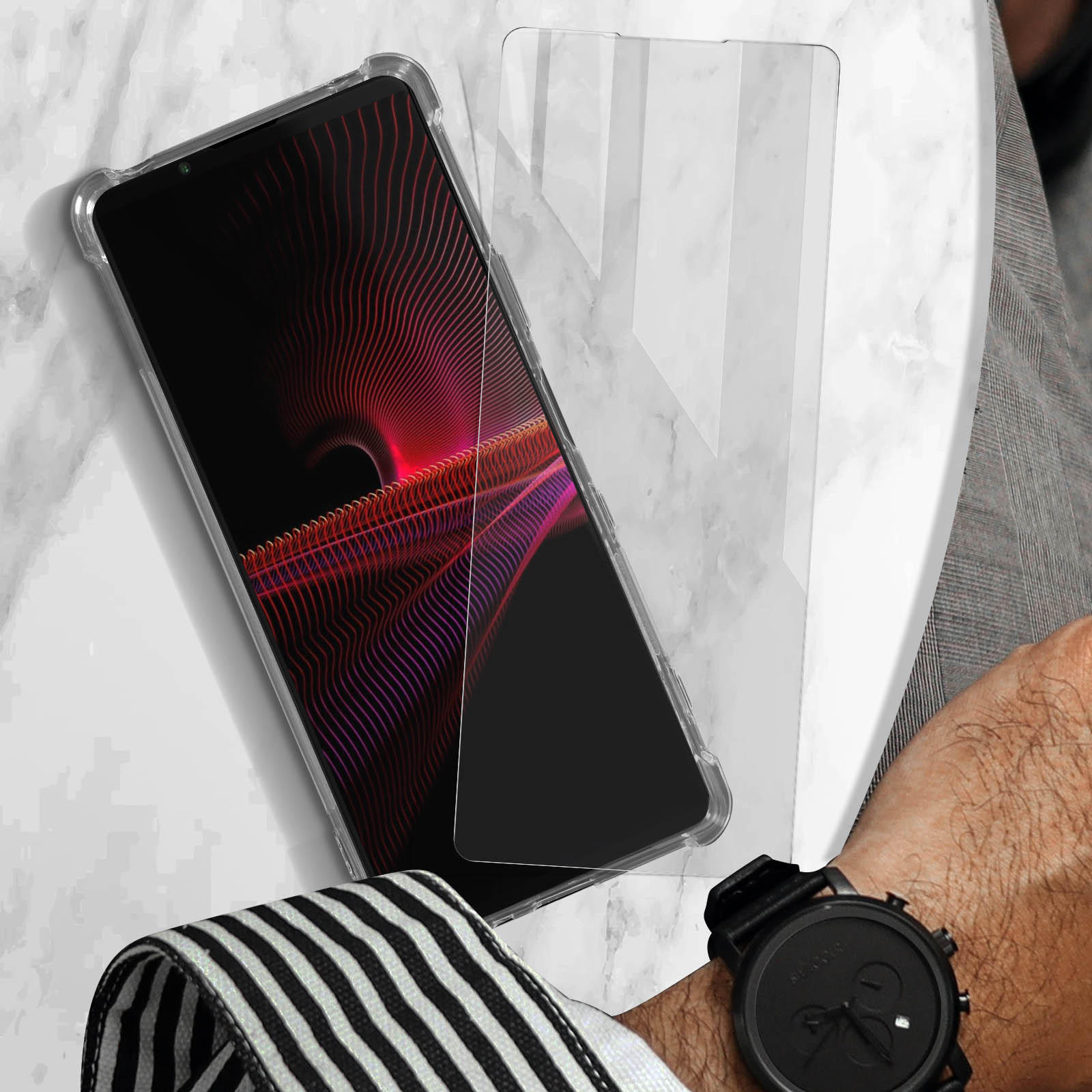 Telefono nero con protezione schermo e un orologio su una superficie di marmo.