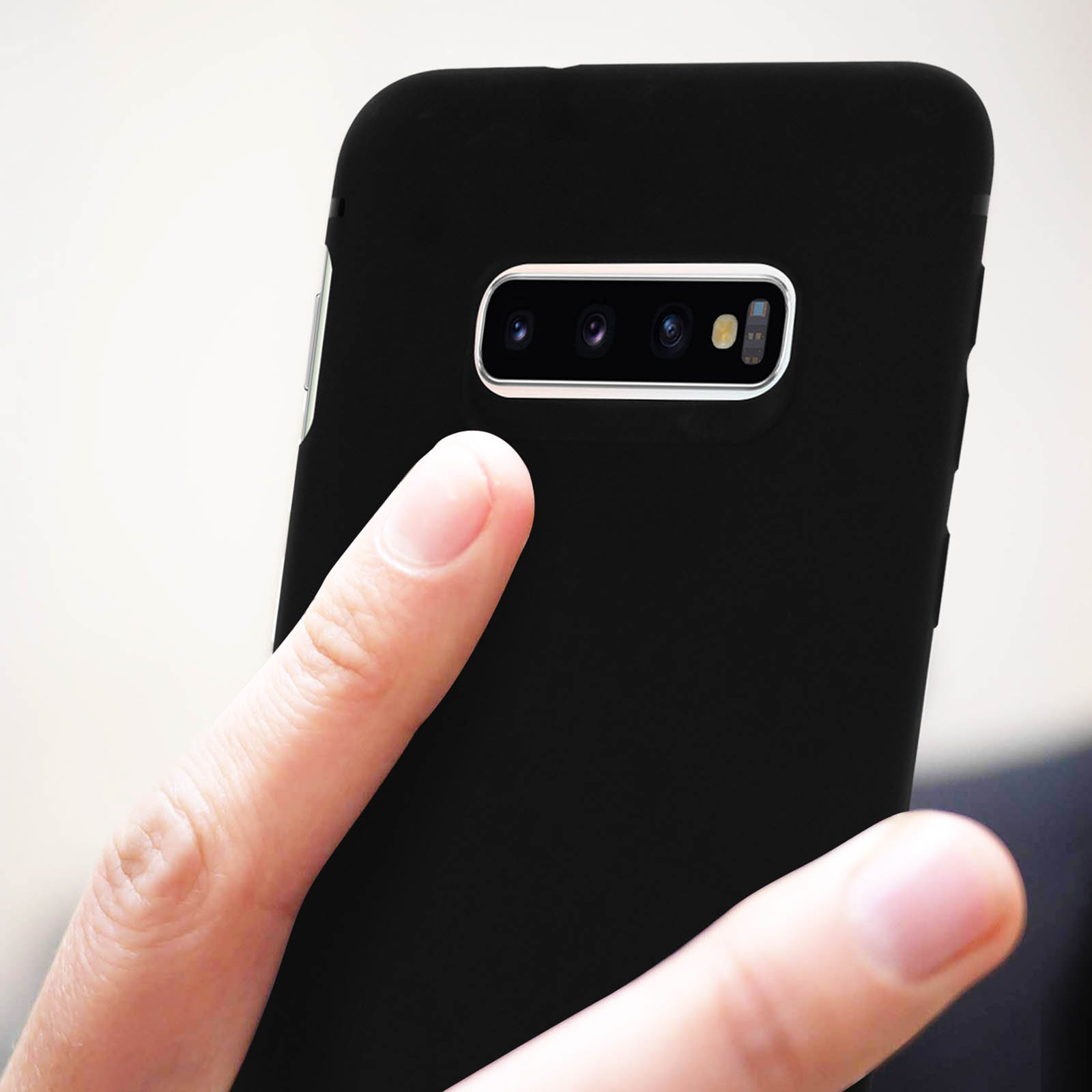 Mano che tiene un telefono nero. La fotocamera del telefono è visibile. Lo sfondo è sfocato.