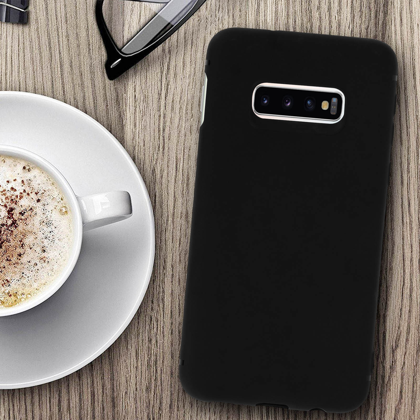 Telefono nero con custodia, accanto a caffè e occhiali su un tavolo di legno.