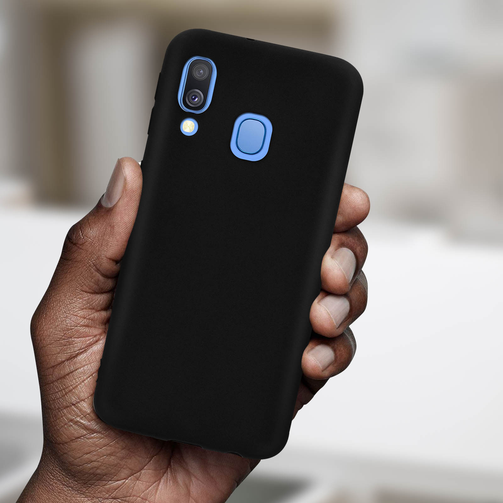 Hand die een zwarte telefoon in een zwarte hoes vasthoudt. De telefoon heeft een blauwe camera en knop.