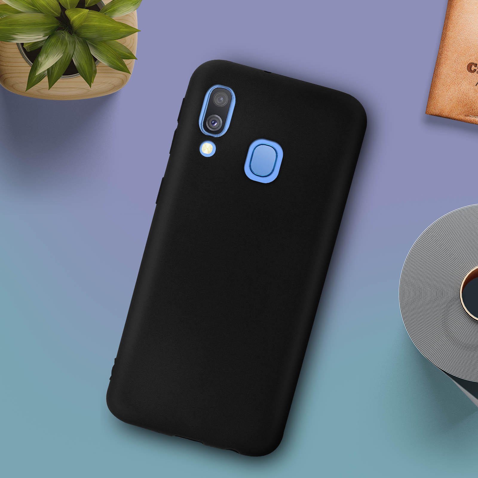 Zwarte telefoonhoes met een telefoon op een blauw oppervlak. Kleine plant en items ernaast.
