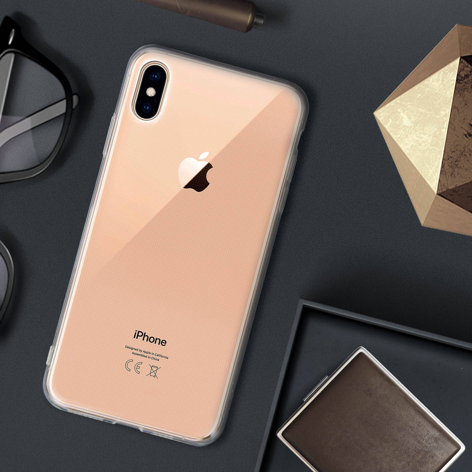 iPhone in custodia trasparente su superficie scura, con occhiali e decorazione vicini.