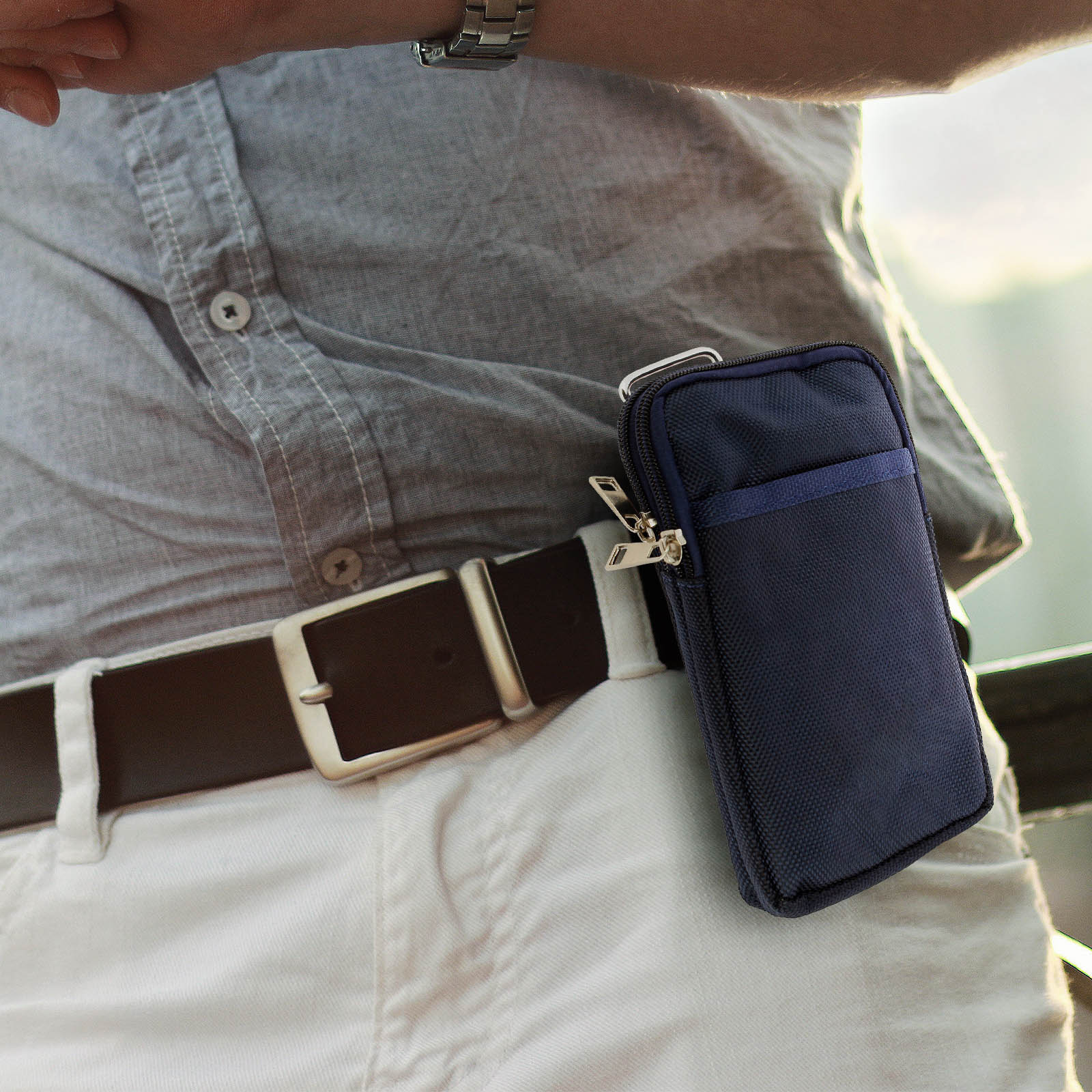 Vita e cintura di un uomo, con una custodia per telefono blu scuro attaccata, cerniera visibile.