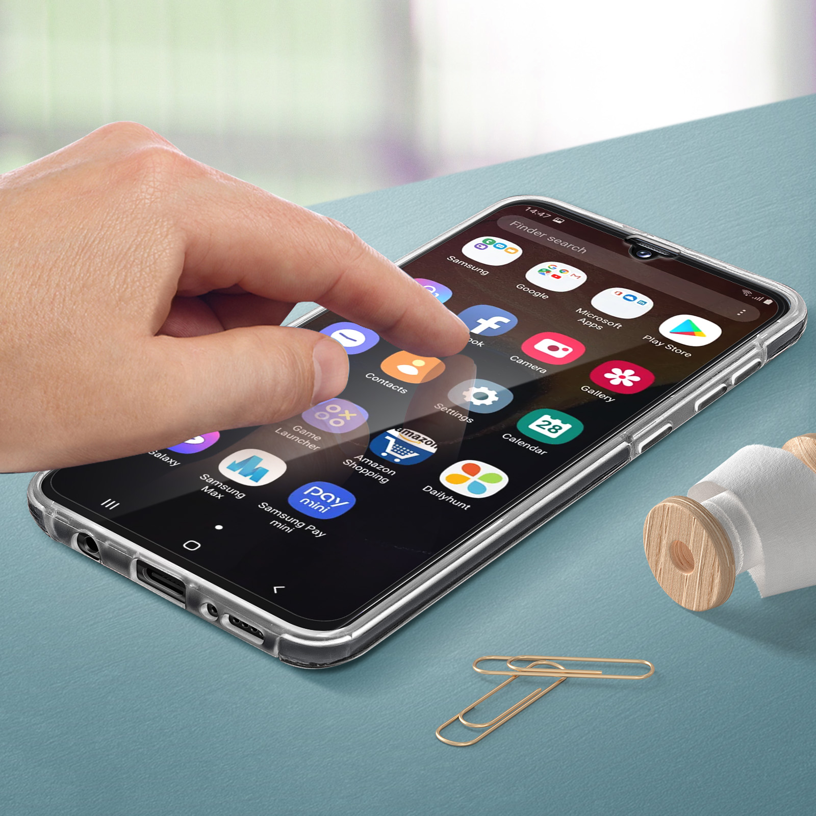 Een hand raakt een telefoonscherm aan met app-pictogrammen. Paperclips en een klein object op de tafel.