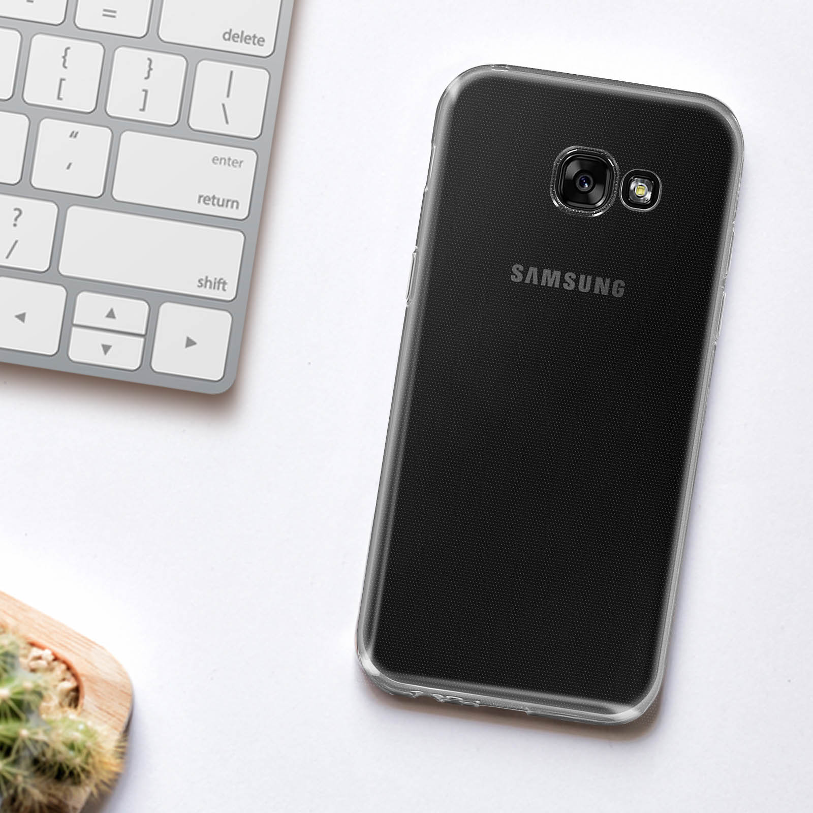 Telefono Samsung in una custodia trasparente su un tavolo. Tastiera e pianta sullo sfondo.
