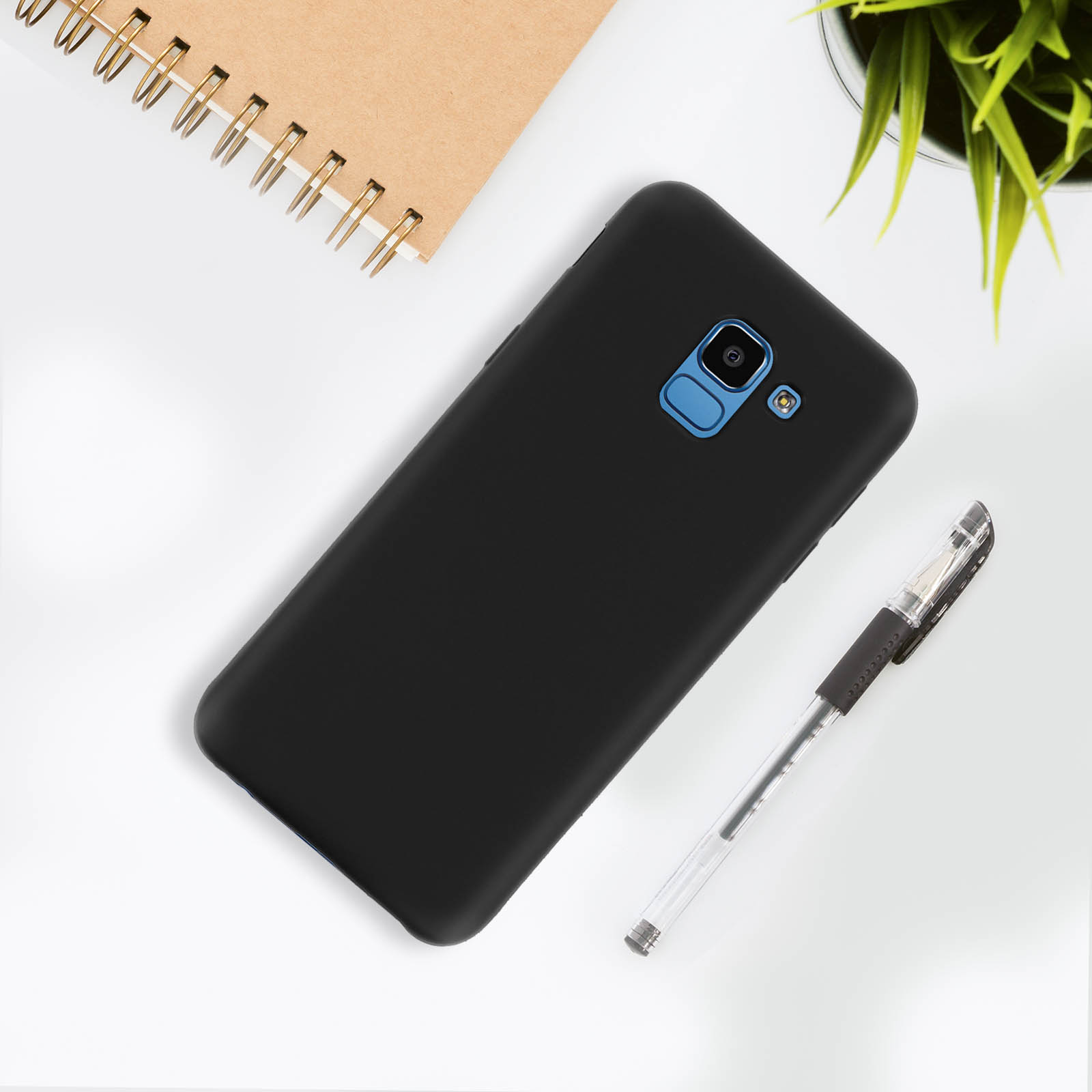 Un telefono nero con una penna nera e un taccuino su una superficie bianca.