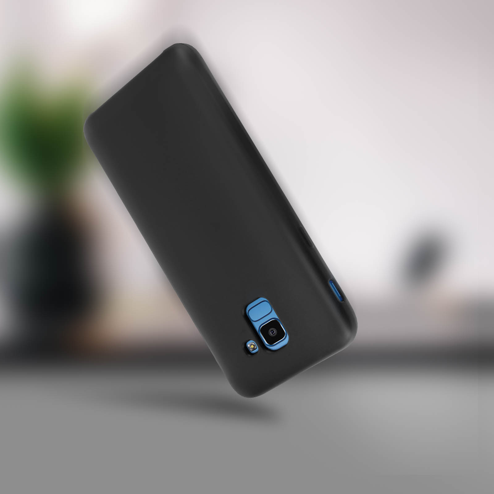 Custodia nera per telefono, angolata, con dettaglio dell'area della fotocamera. Sfondo sfocato con pianta.