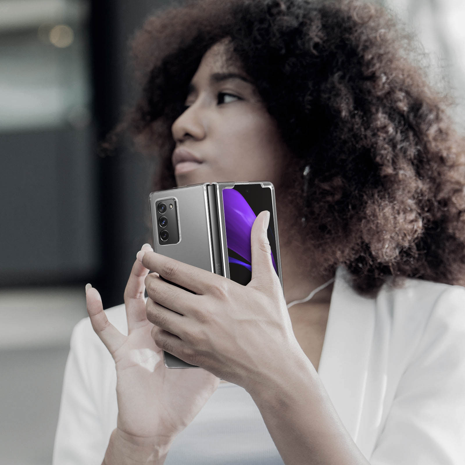 Donna che tiene in mano un telefono grigio pieghevole, parzialmente aperto, su sfondo sfocato.
